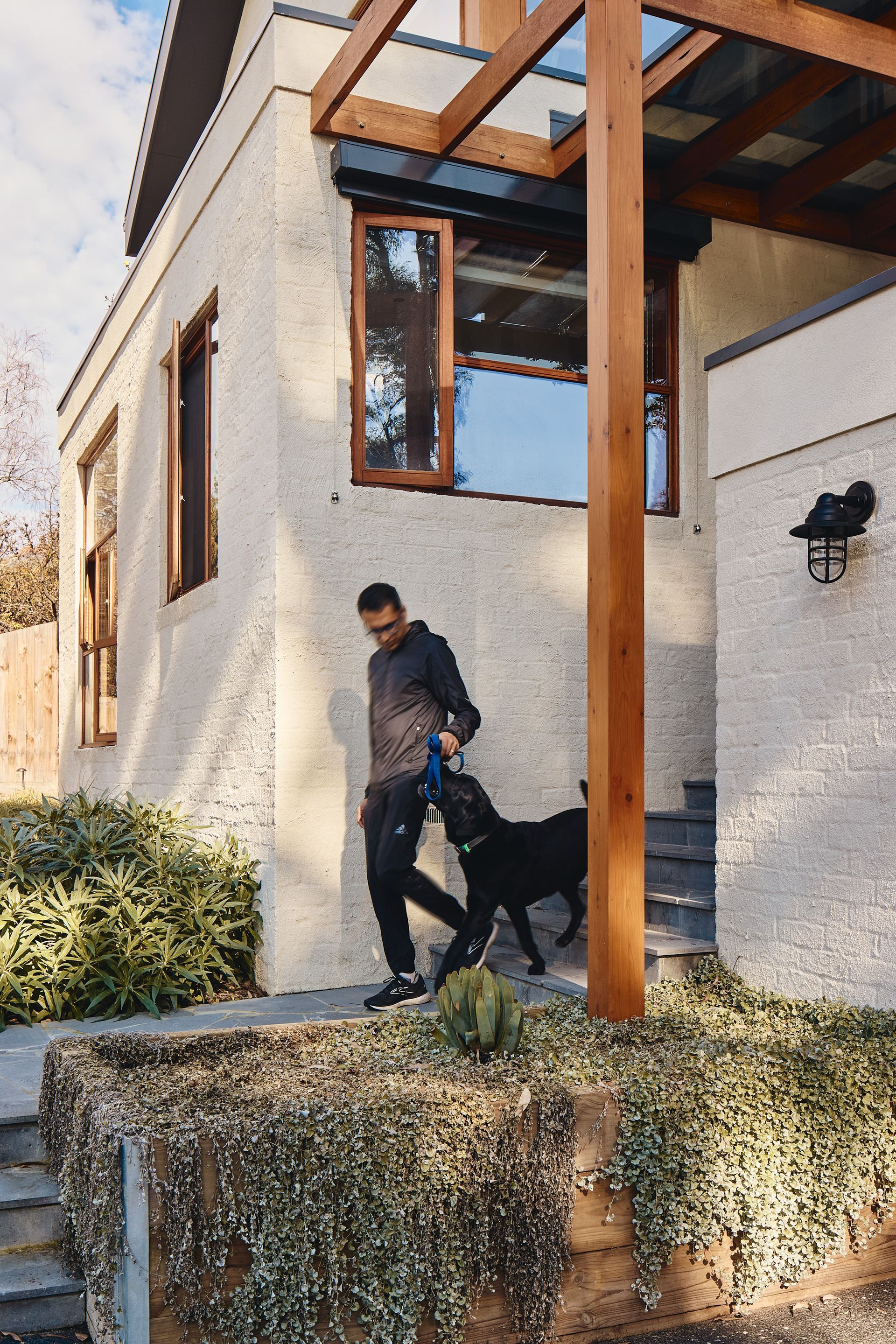 A man is walking a dog on a leash in front of a house.