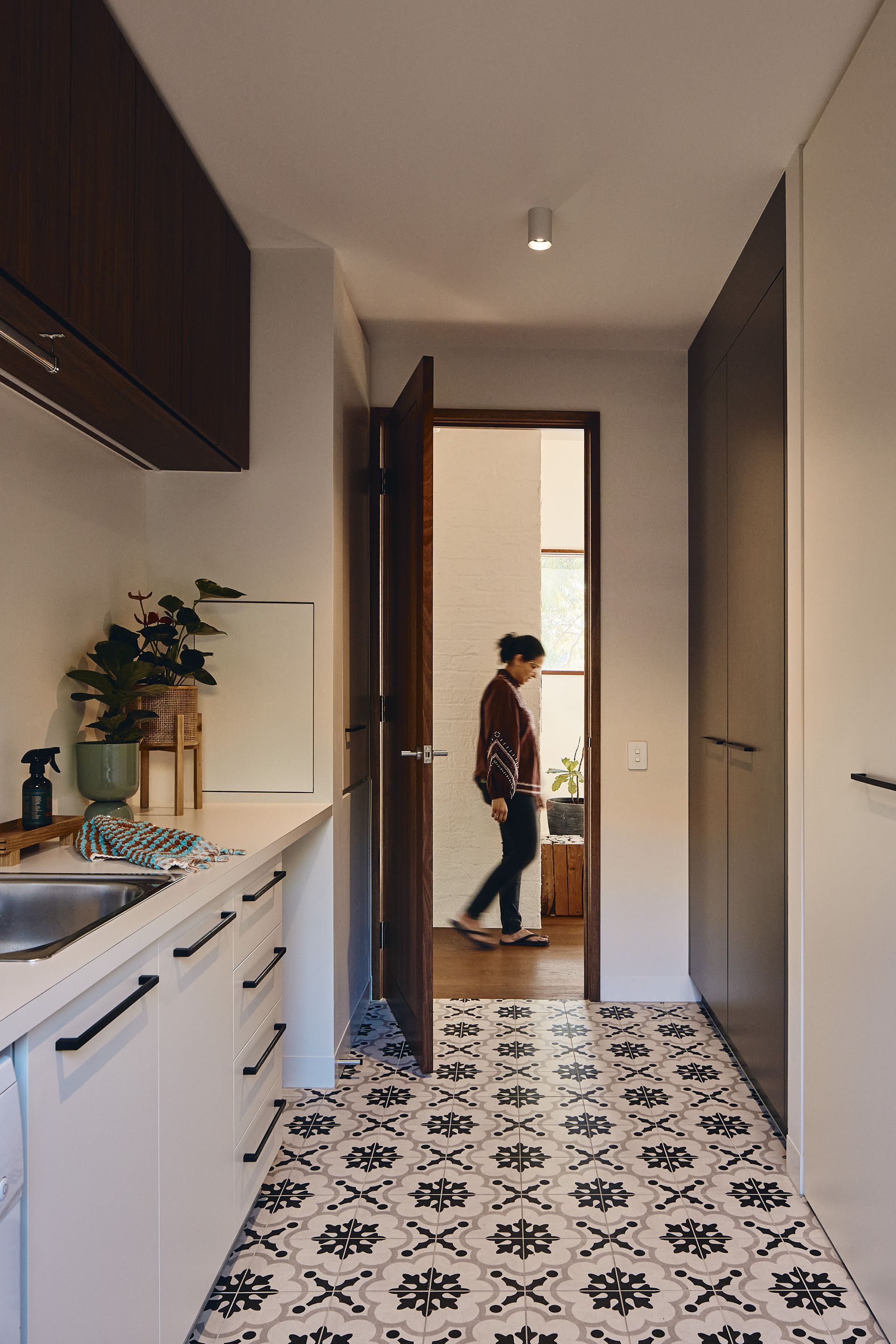 A woman is walking down a hallway in a kitchen.