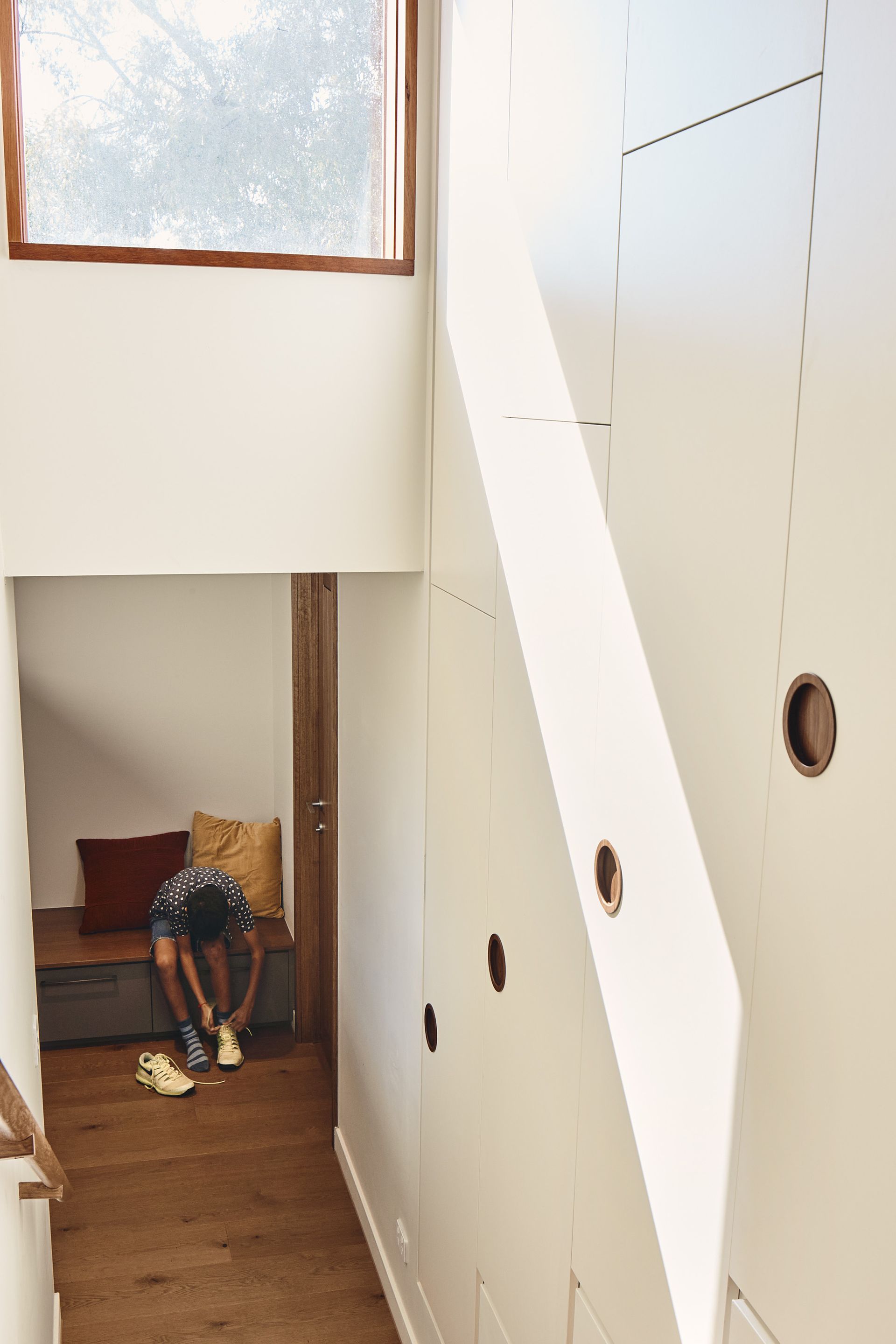 A person is sitting on a bench under the stairs in a hallway.