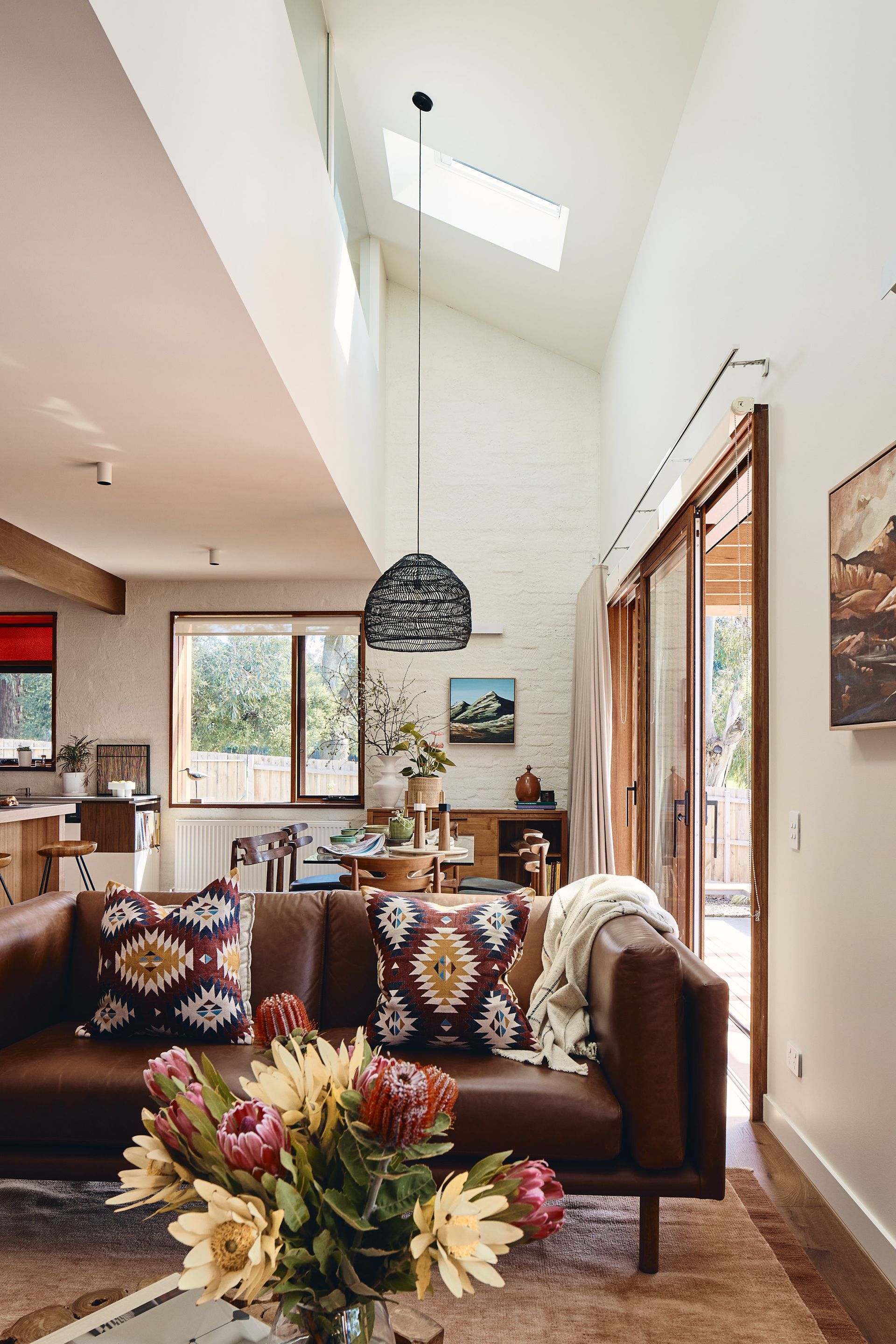 A living room with a brown couch and a vase of flowers on the table.