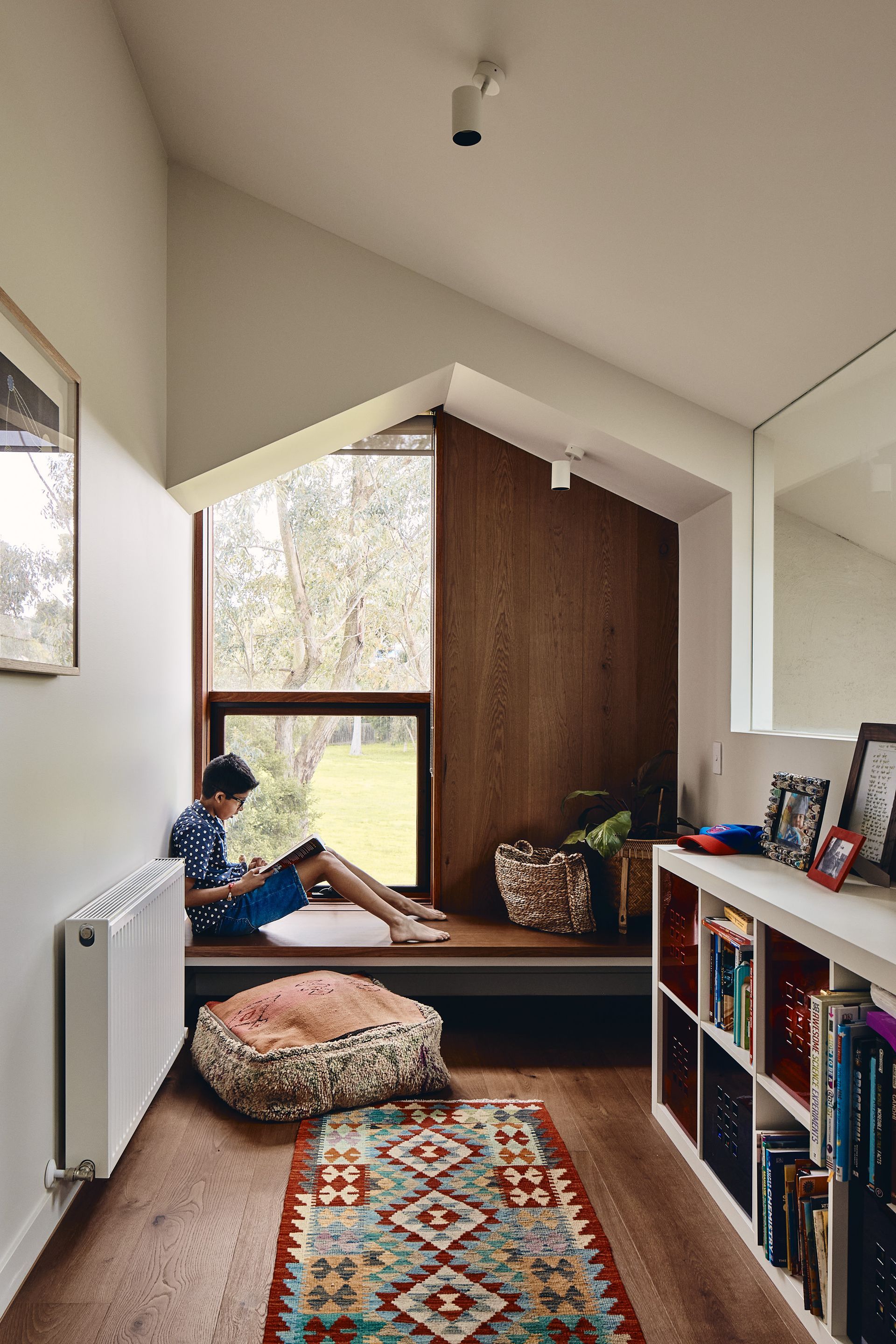 A boy is sitting on a window sill reading a book.