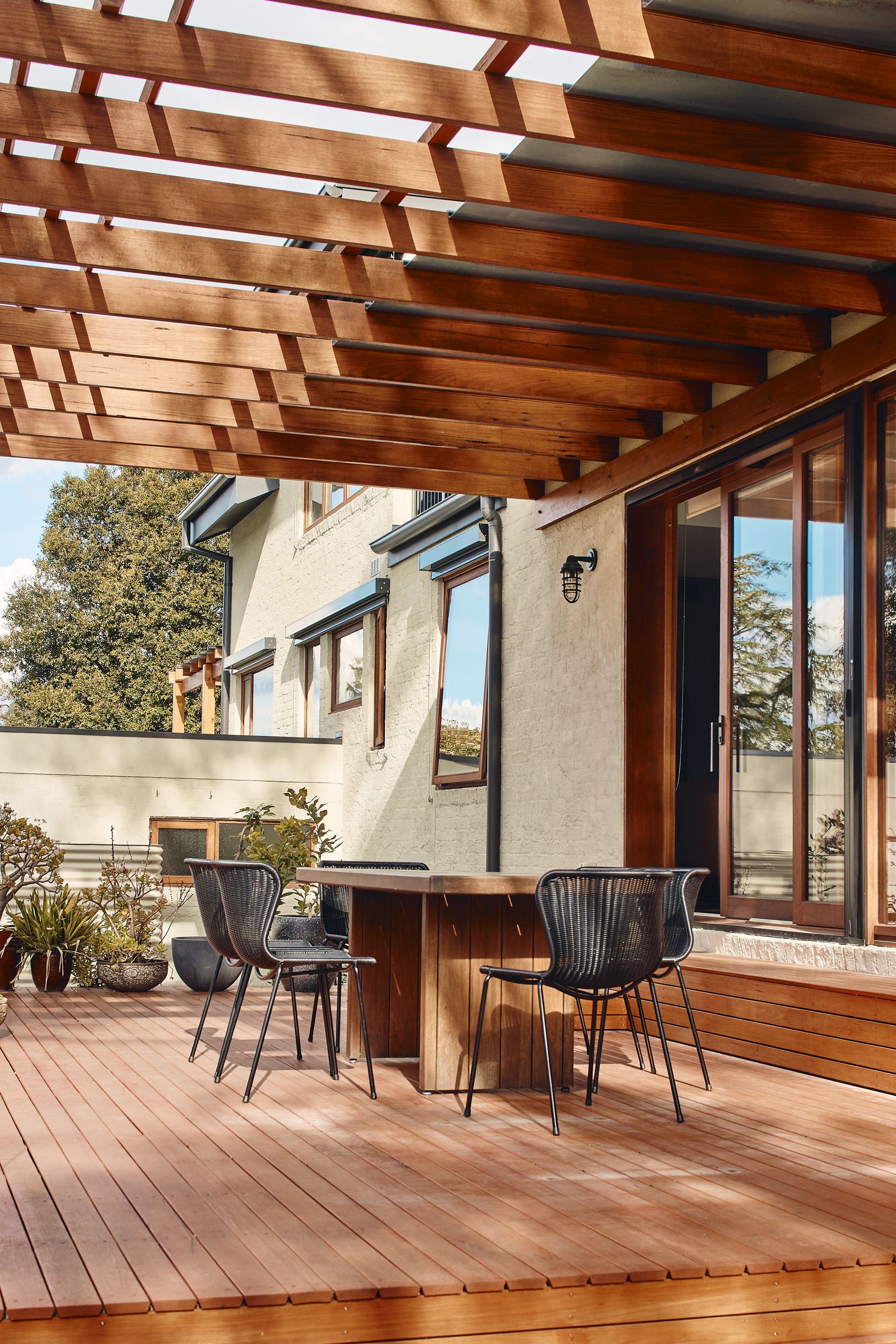 A wooden deck with a table and chairs under a pergola.