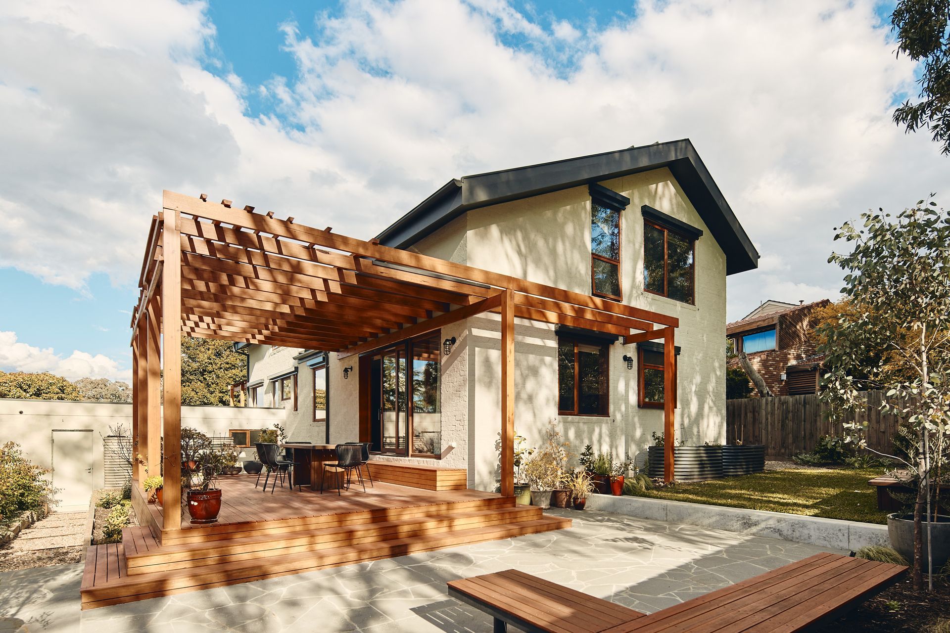 A white house with a wooden pergola in front of it.