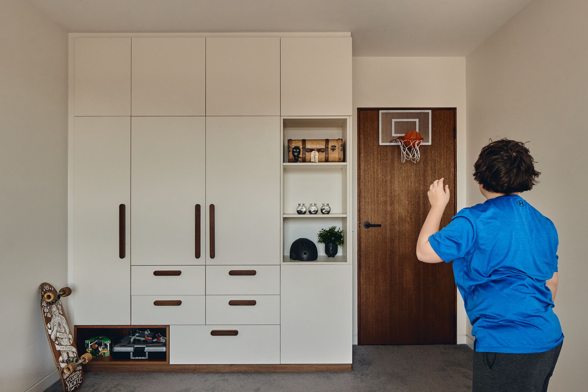 A man in a blue shirt is playing basketball in a bedroom.