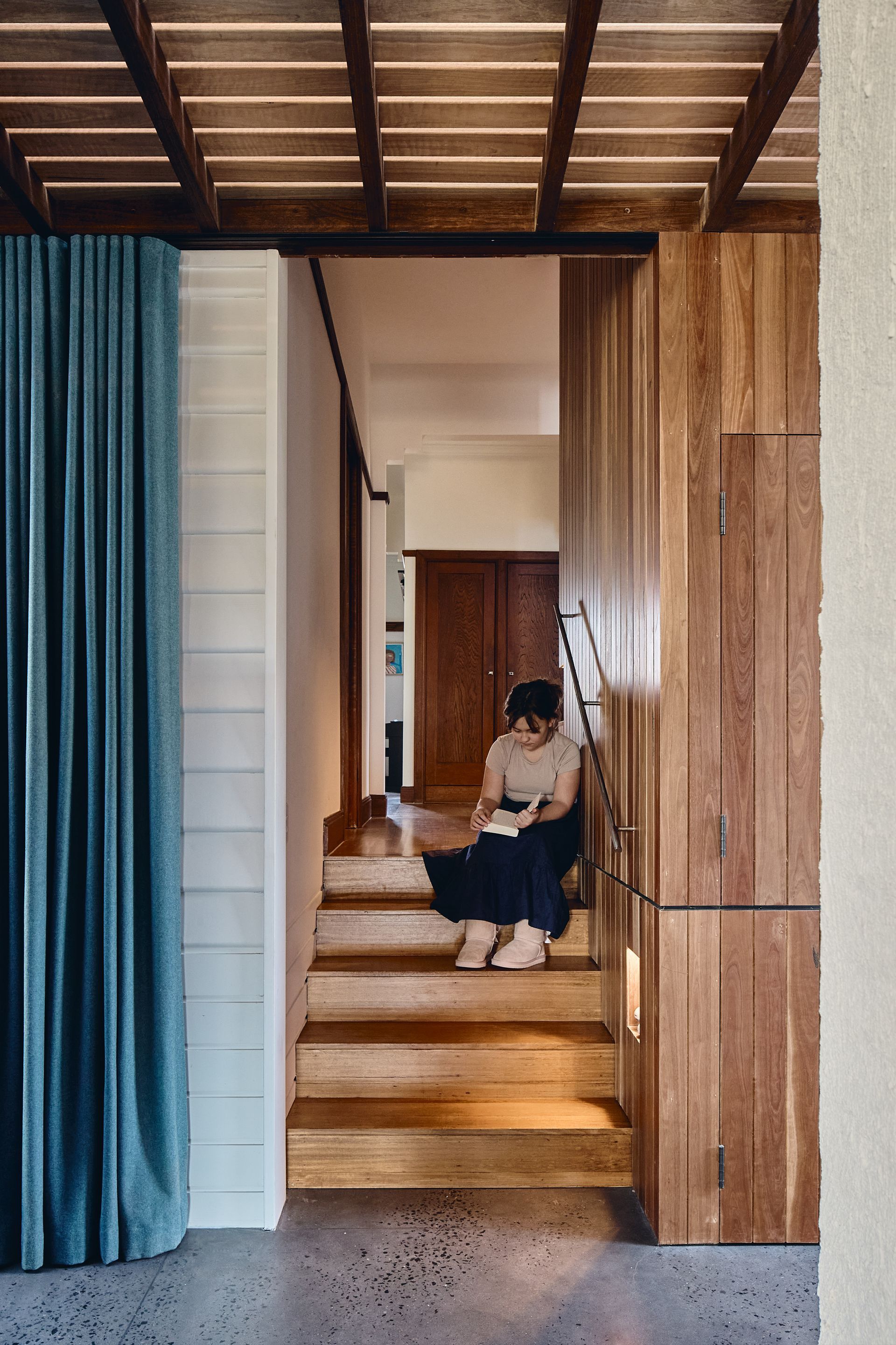 A woman is sitting on the stairs of a house reading a book.