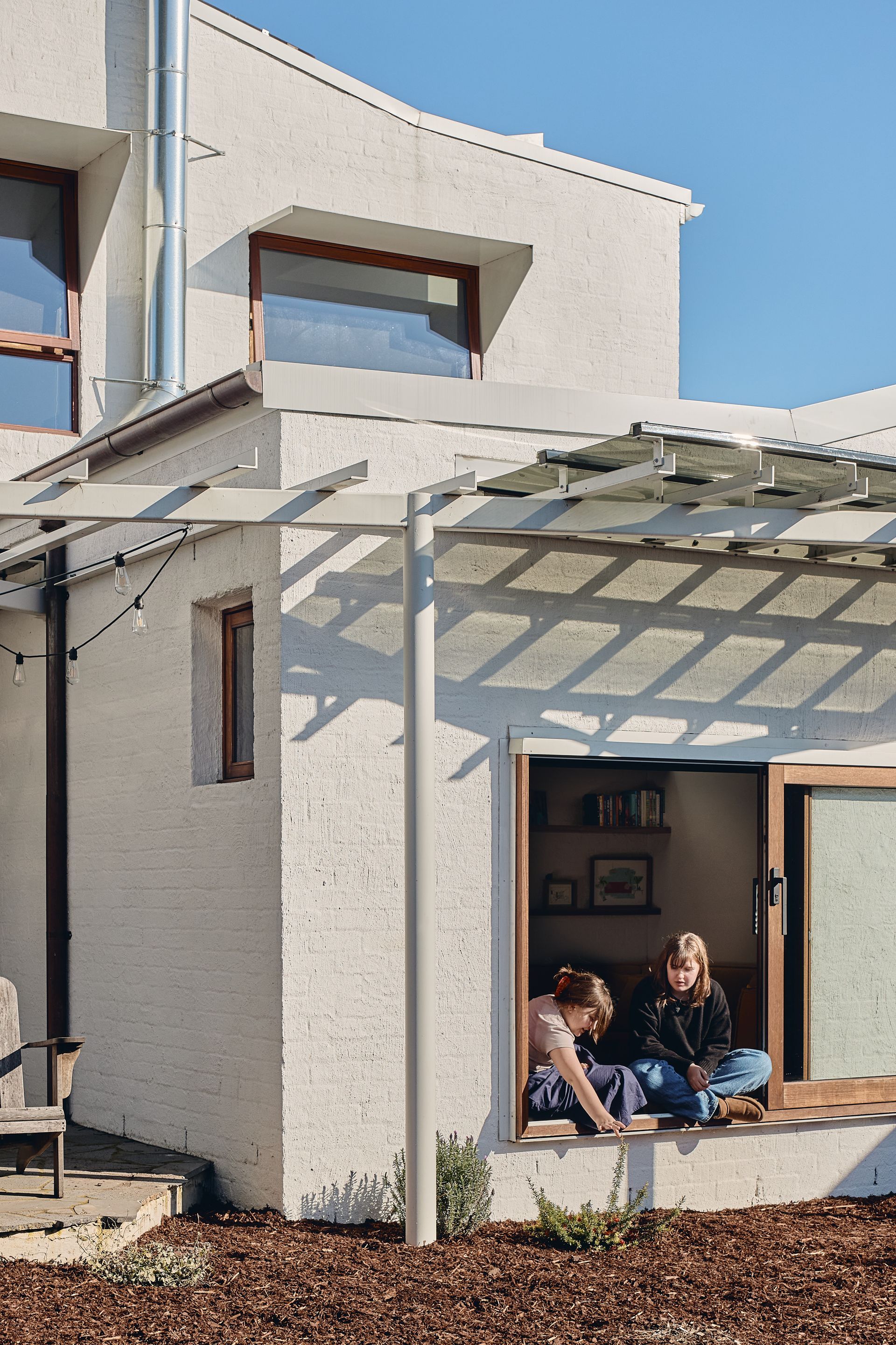 Two people are sitting on a window sill in front of a house.