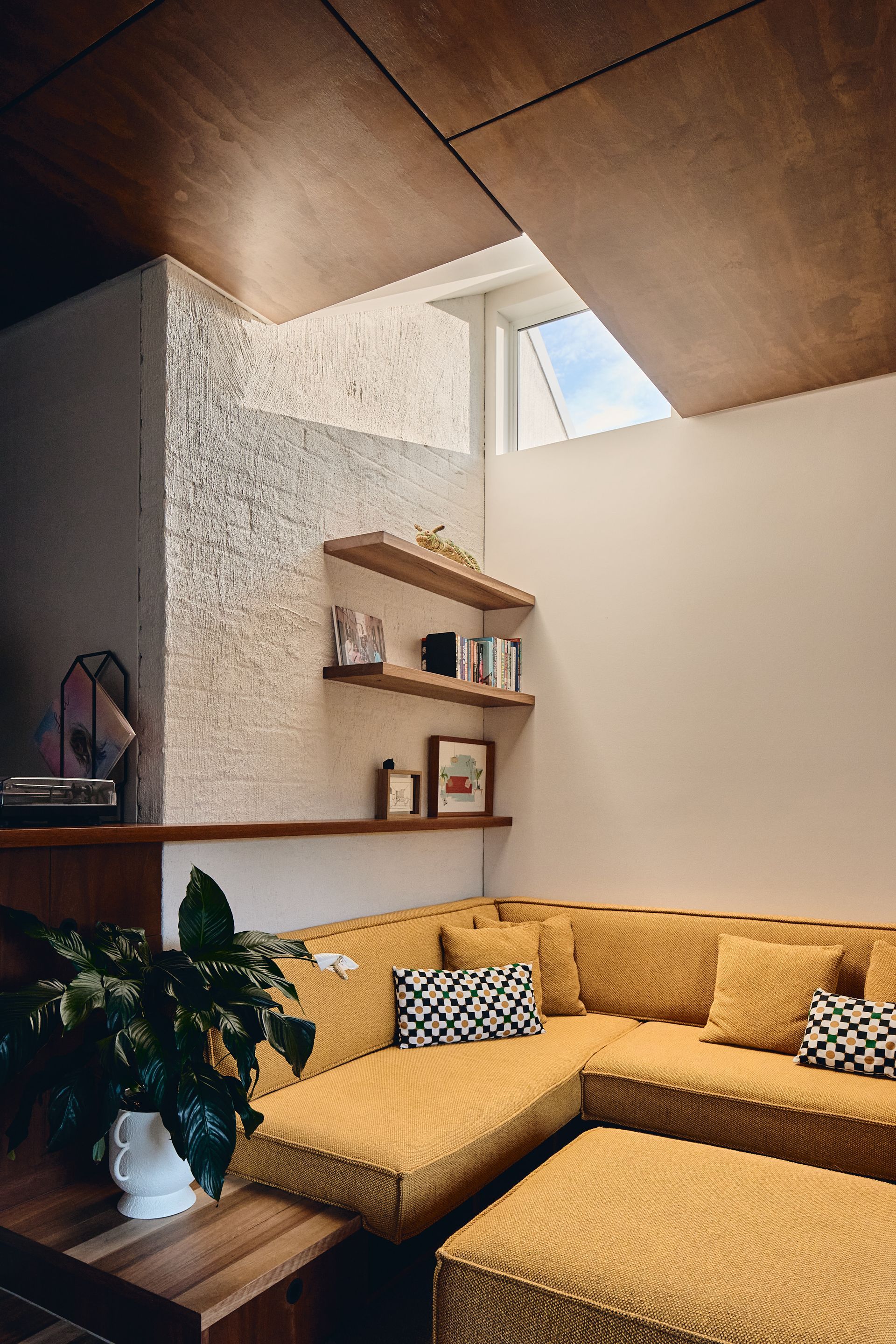 A living room with a yellow sectional couch and ottoman.