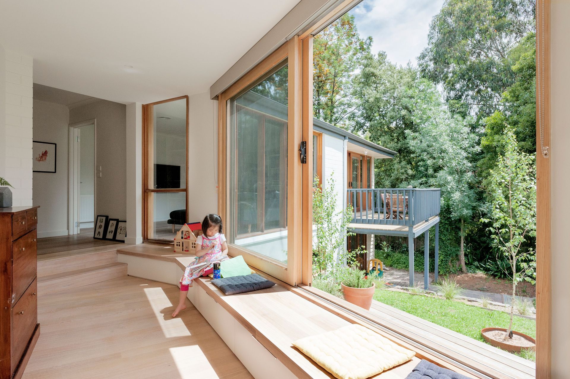 A little girl is sitting on a window sill in a living room