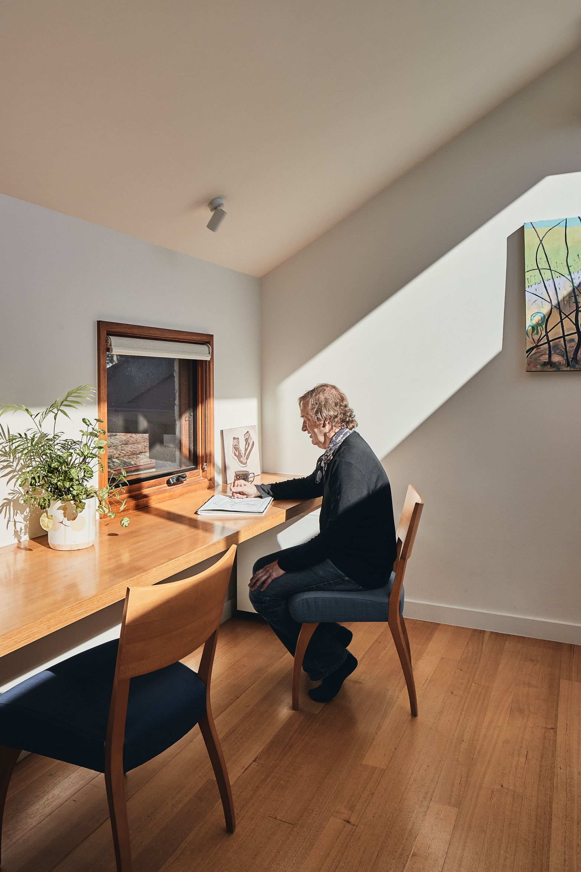 A man is sitting at a desk in a room with a window.