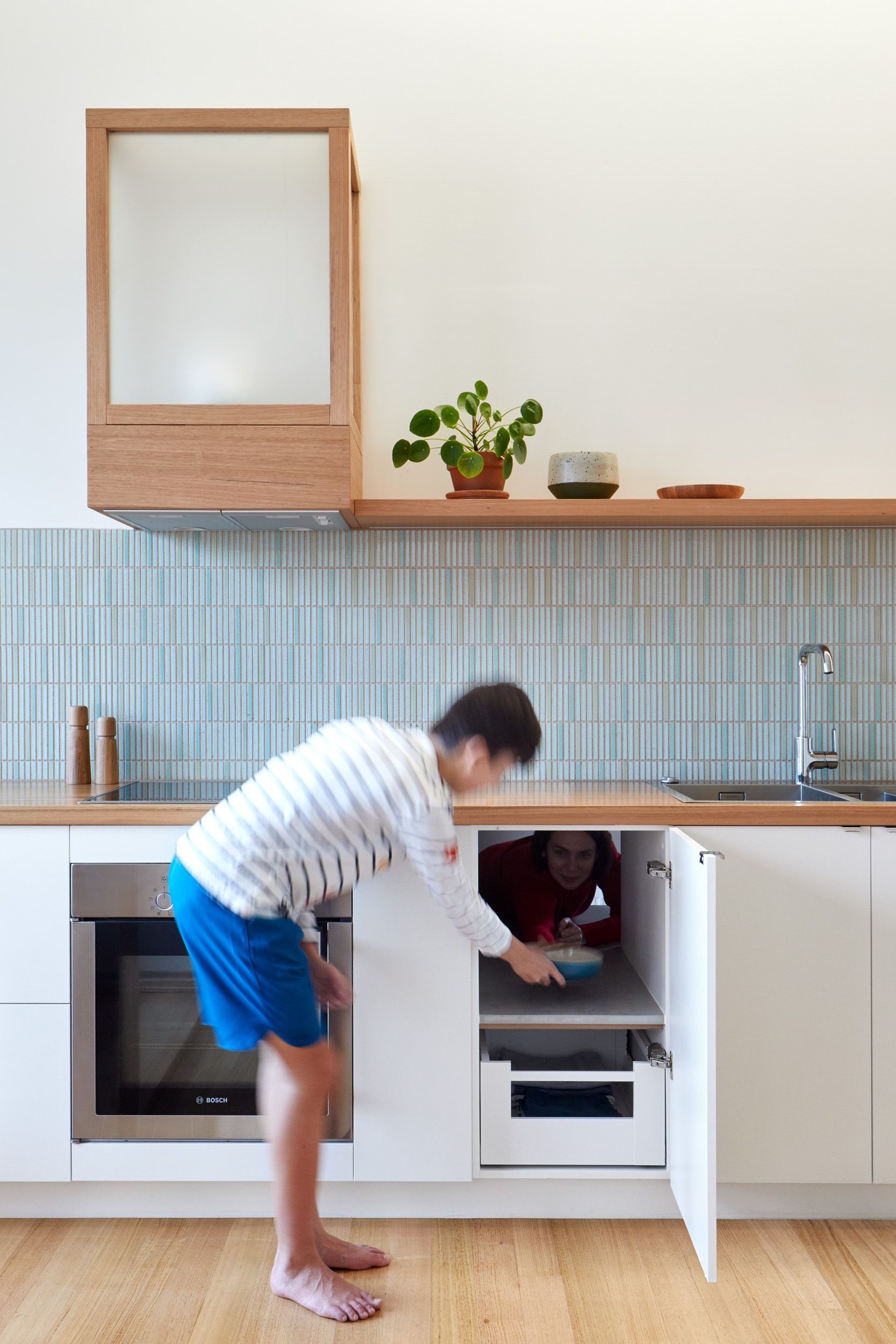 A man is standing in a kitchen looking into a cabinet.
