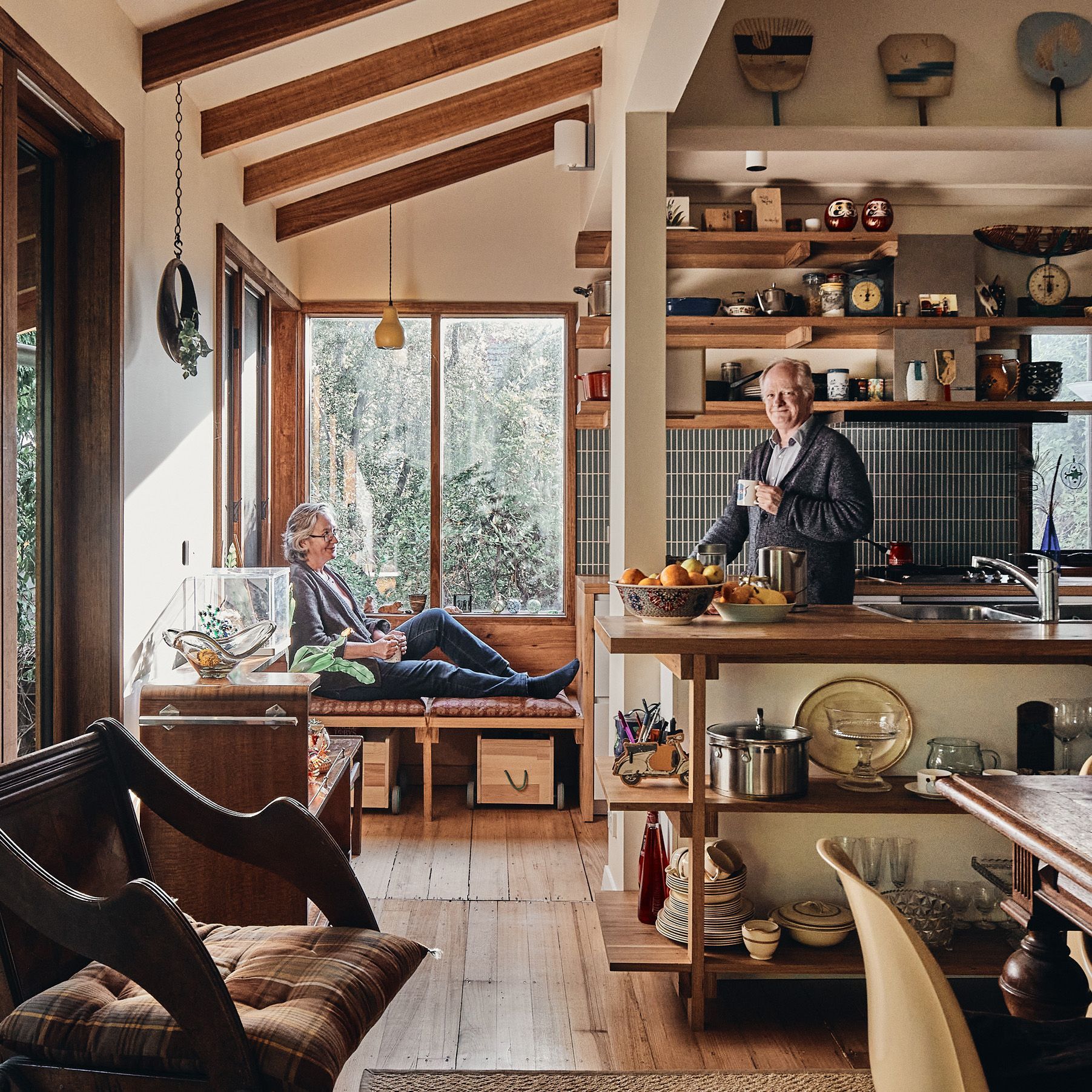 A man sits on a bench in a kitchen while a woman sits on a bench in a living room