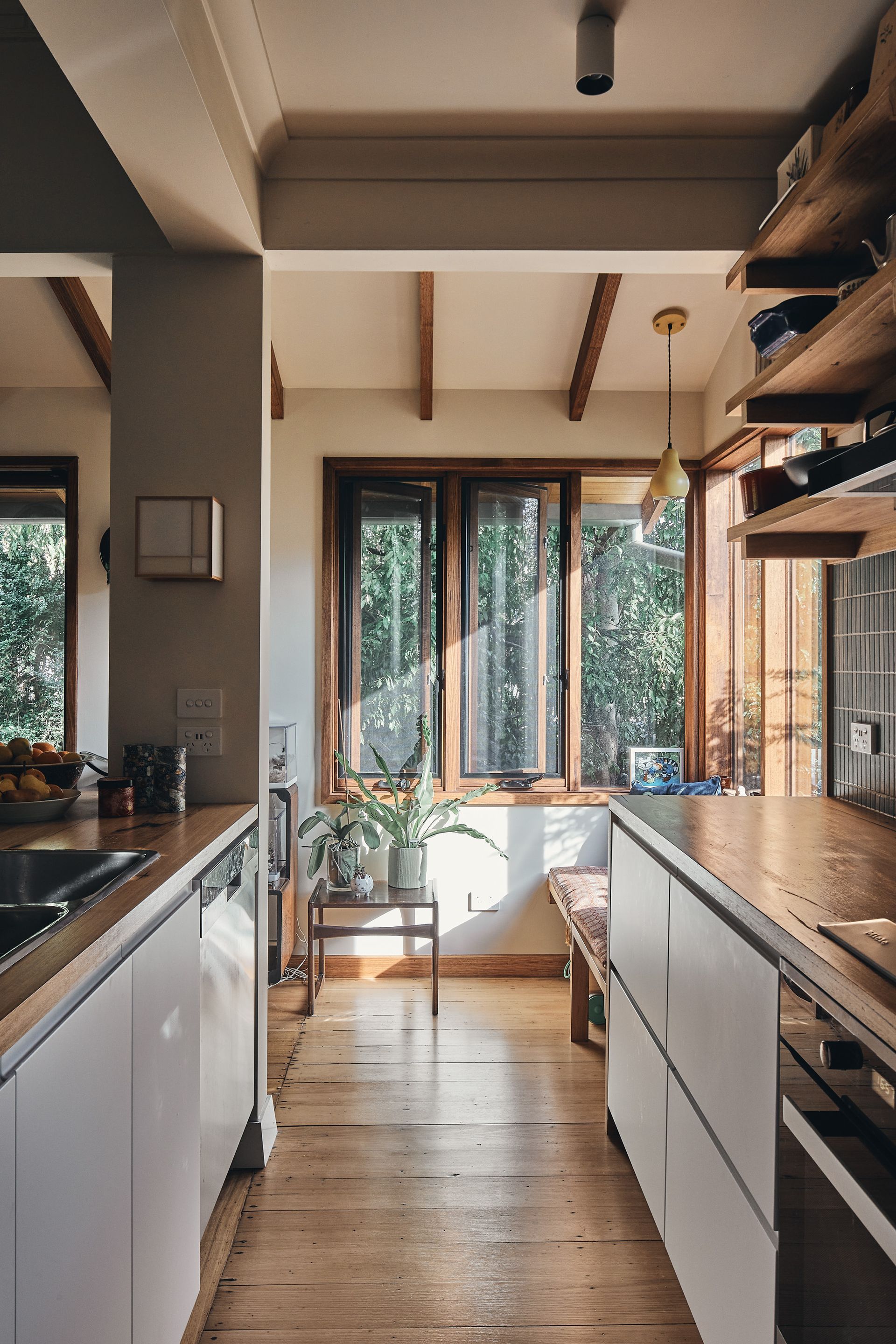 A kitchen with wooden floors , white cabinets , a sink and a window.