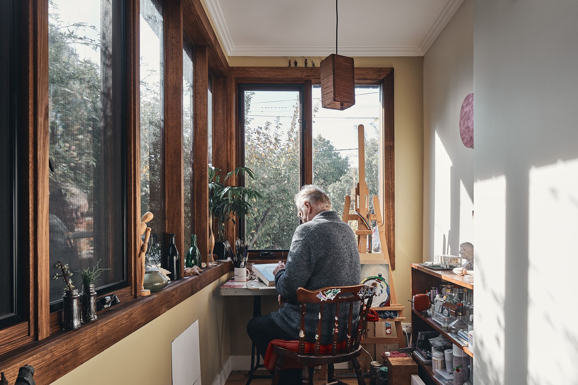 A man is sitting at a desk in a room with a lot of windows.