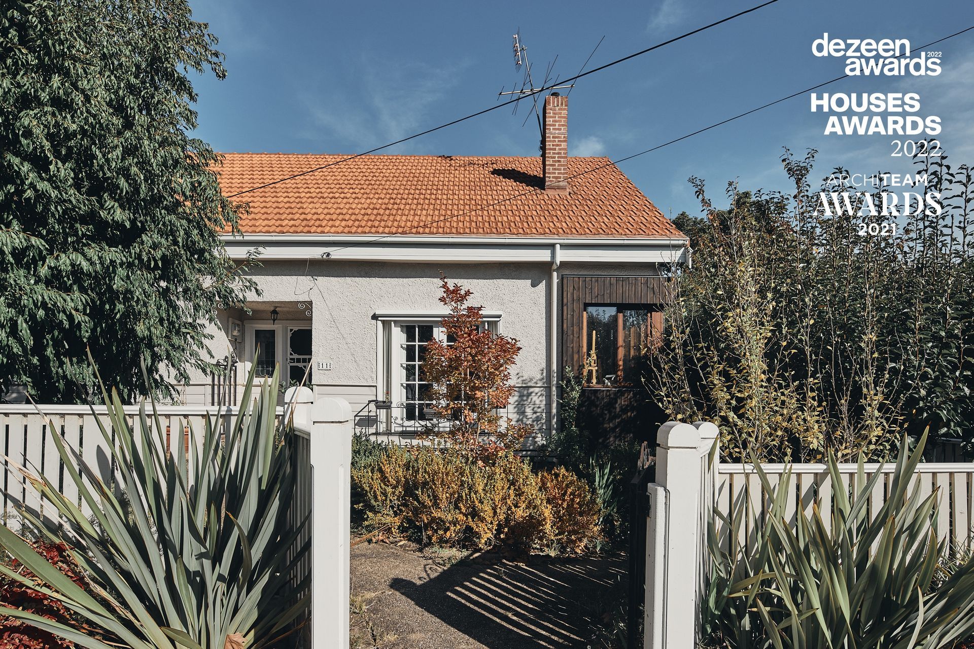 A white house with a red tile roof is surrounded by trees and bushes.