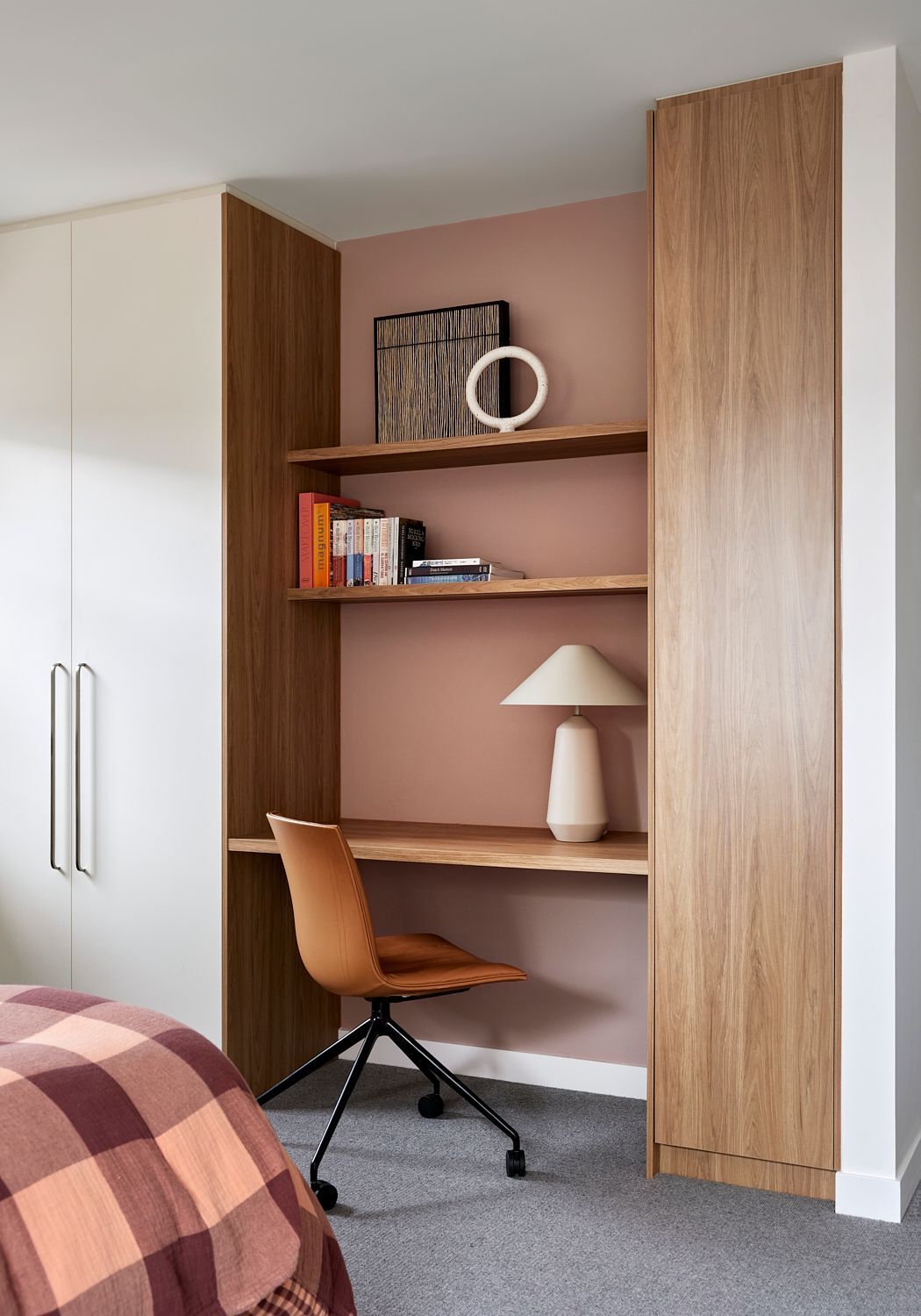 A bedroom with a desk , chair , shelves and a lamp.
