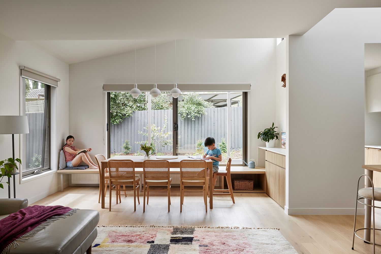 A woman is sitting on a bench in a living room next to a dining table.