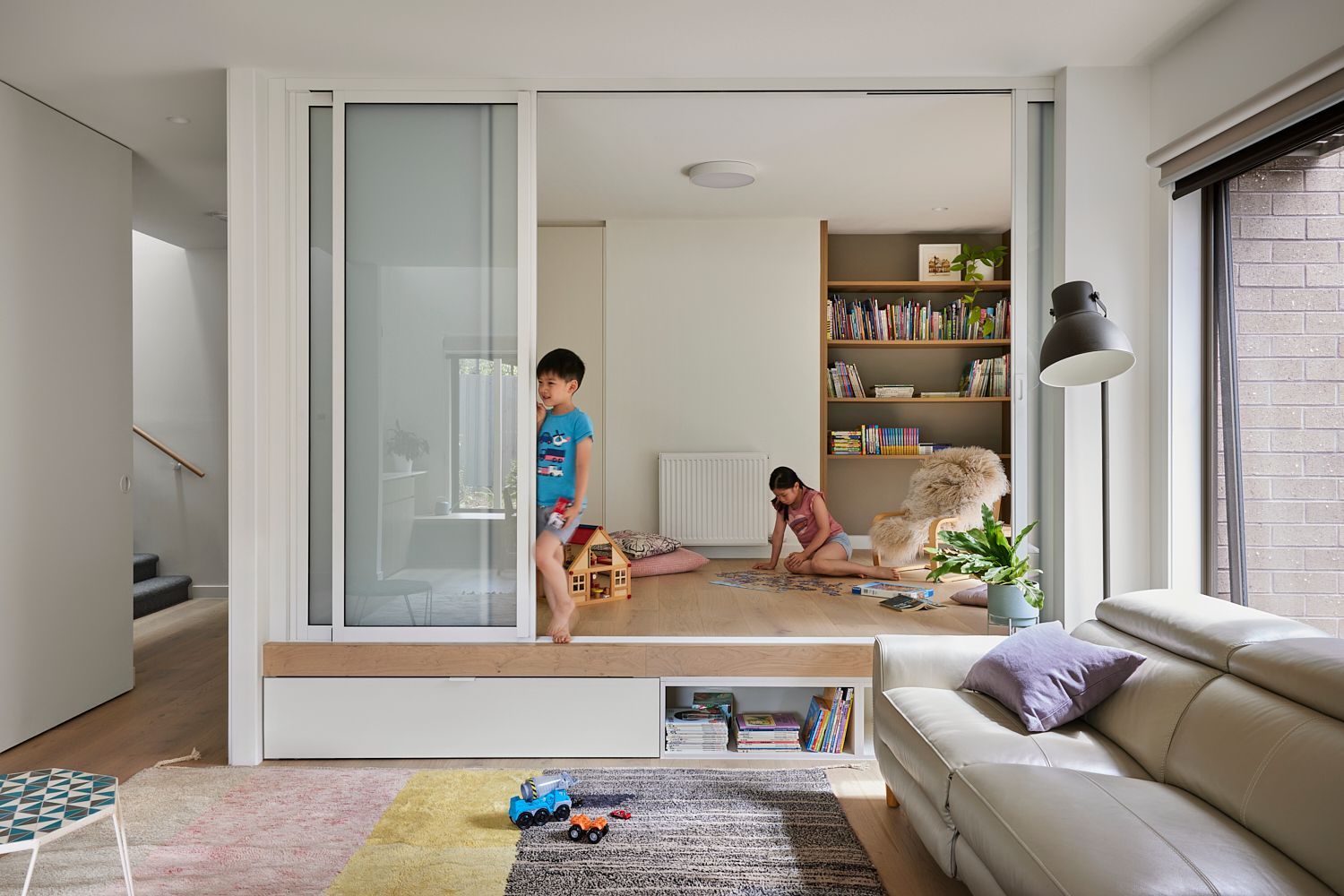 Two children are playing in a living room with a sliding glass door.