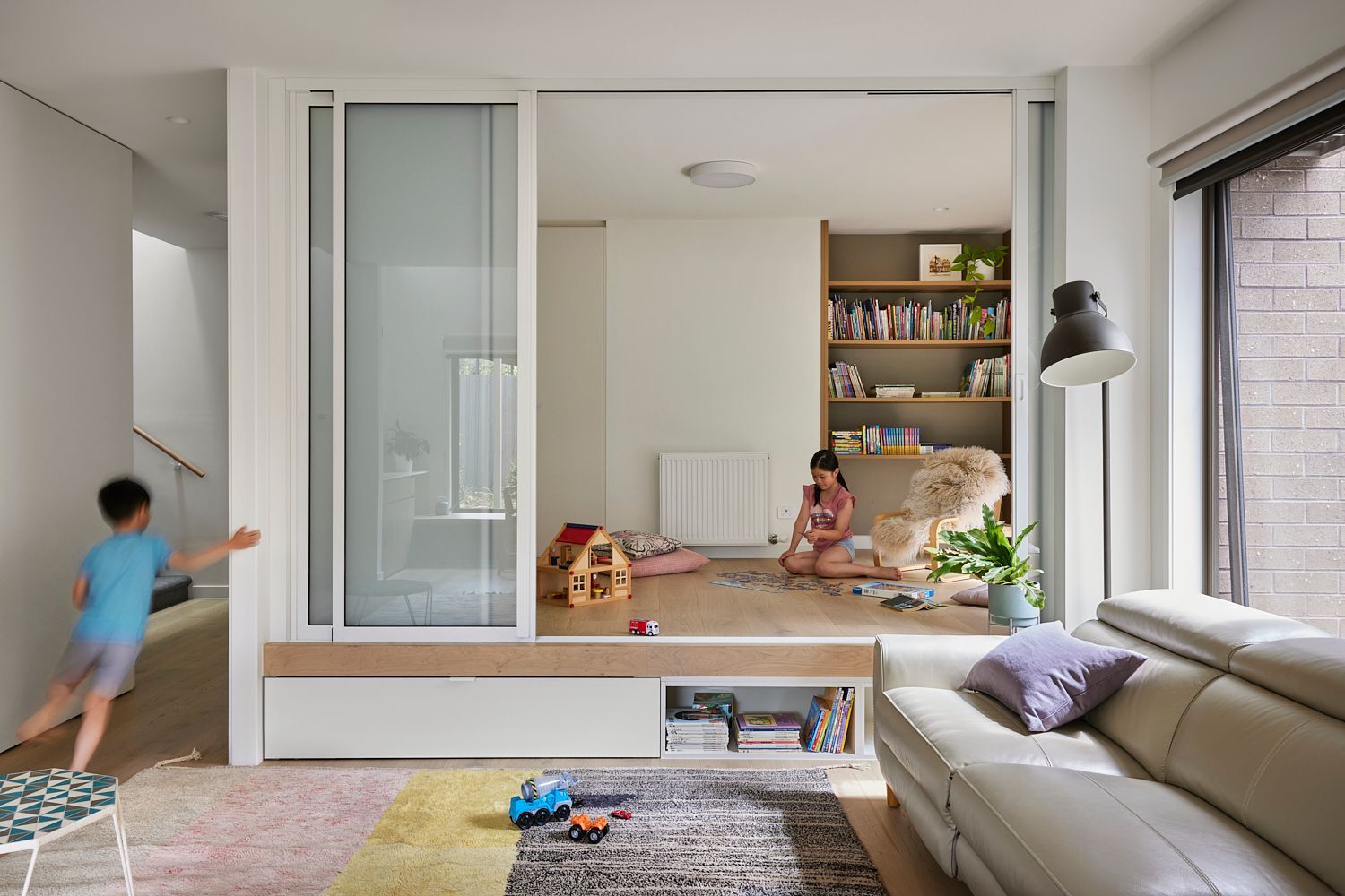 Two children are playing in a living room with a couch and a bookshelf.