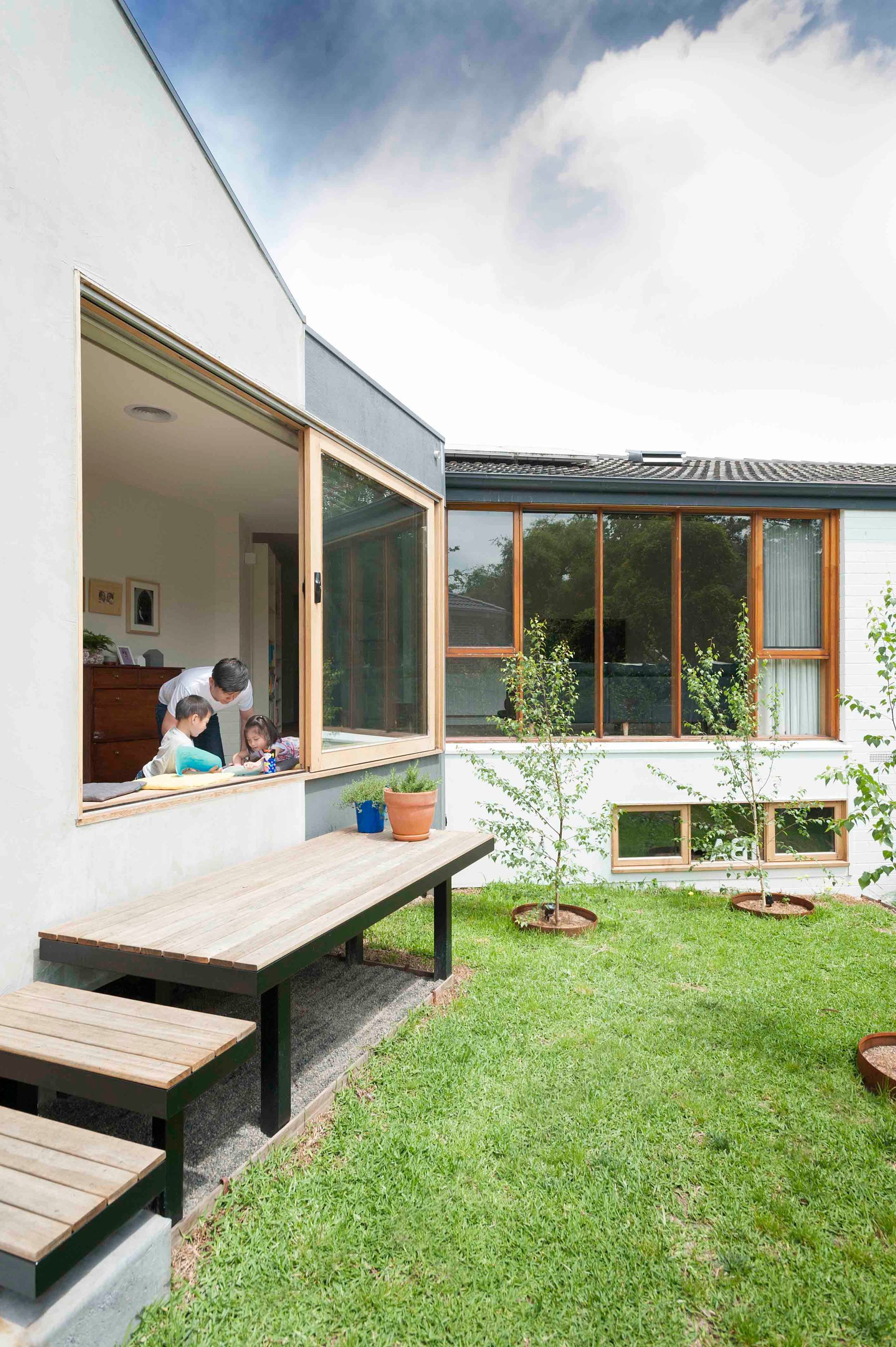 A family is sitting on a bench in the backyard of a house.