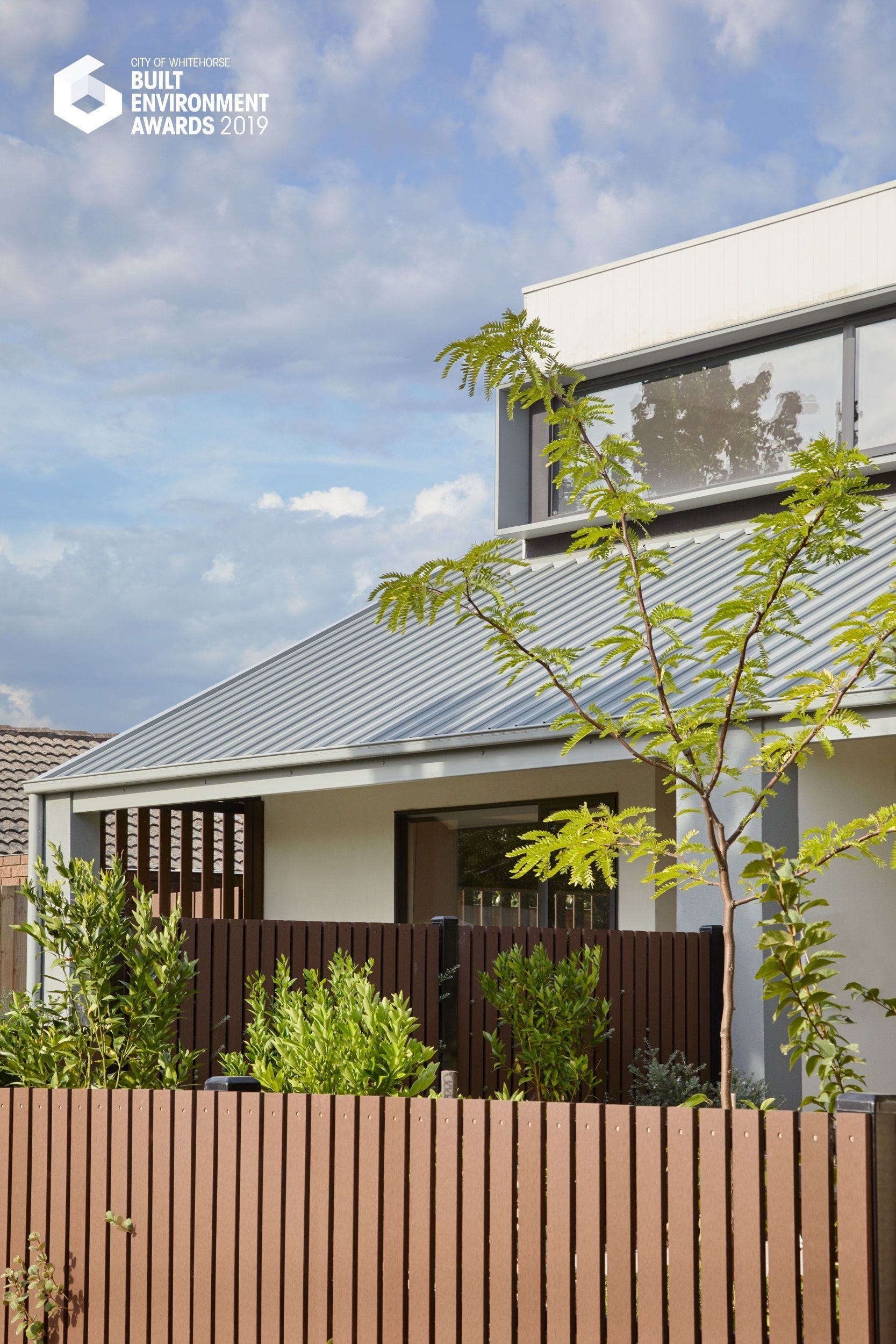 A house with a wooden fence and a tree in front of it.