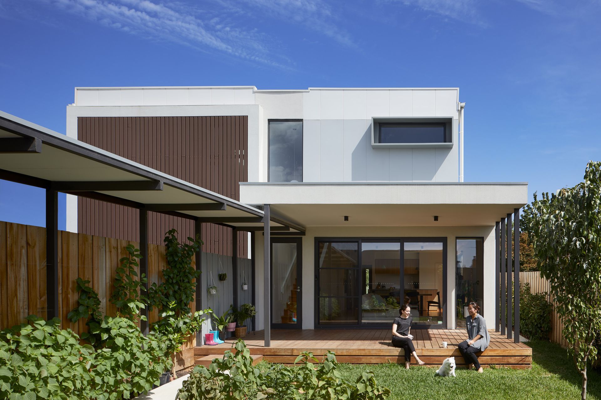 A couple of people are sitting on a deck in front of a house.