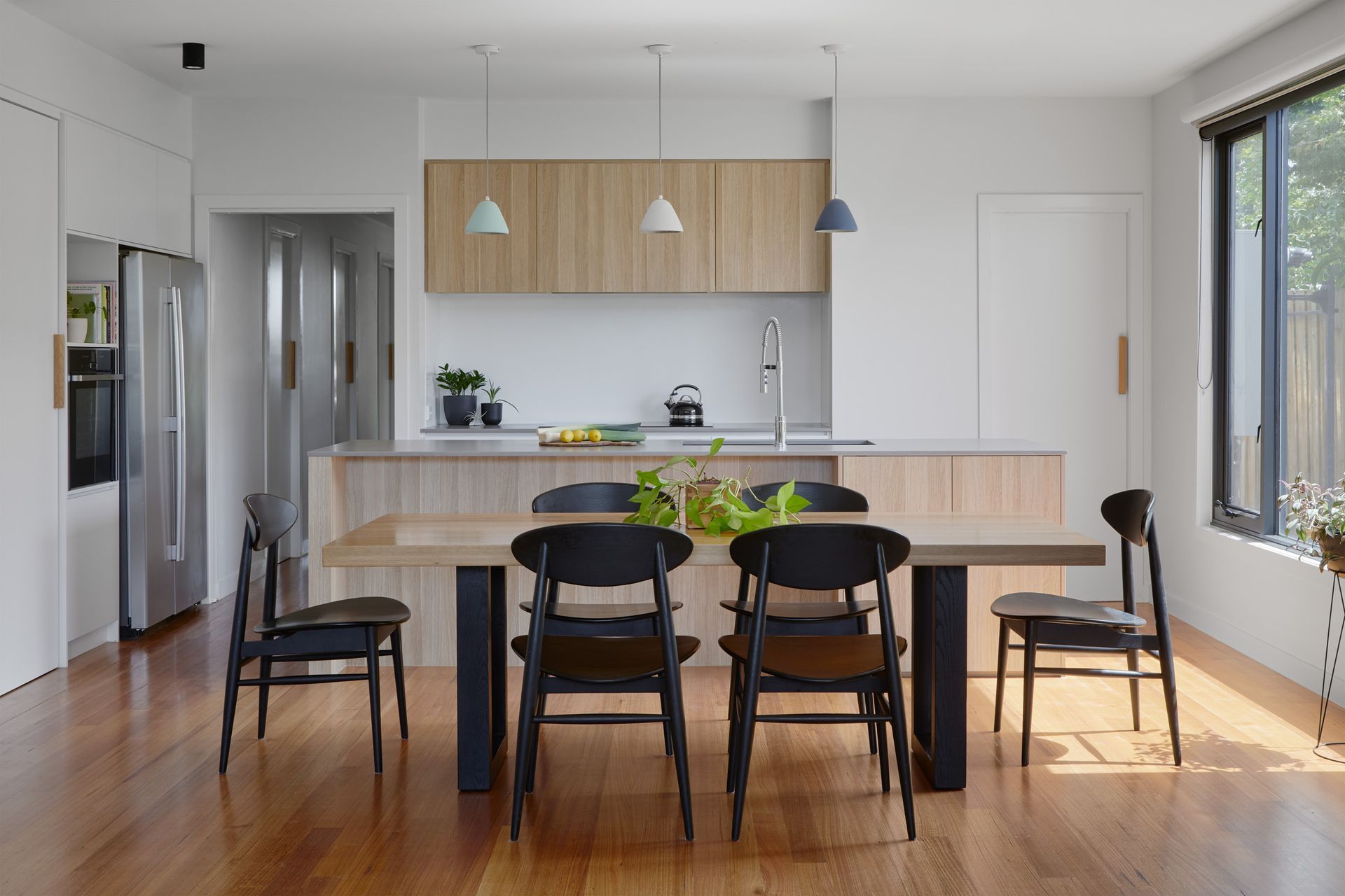 A dining room with a table and chairs and a kitchen in the background.