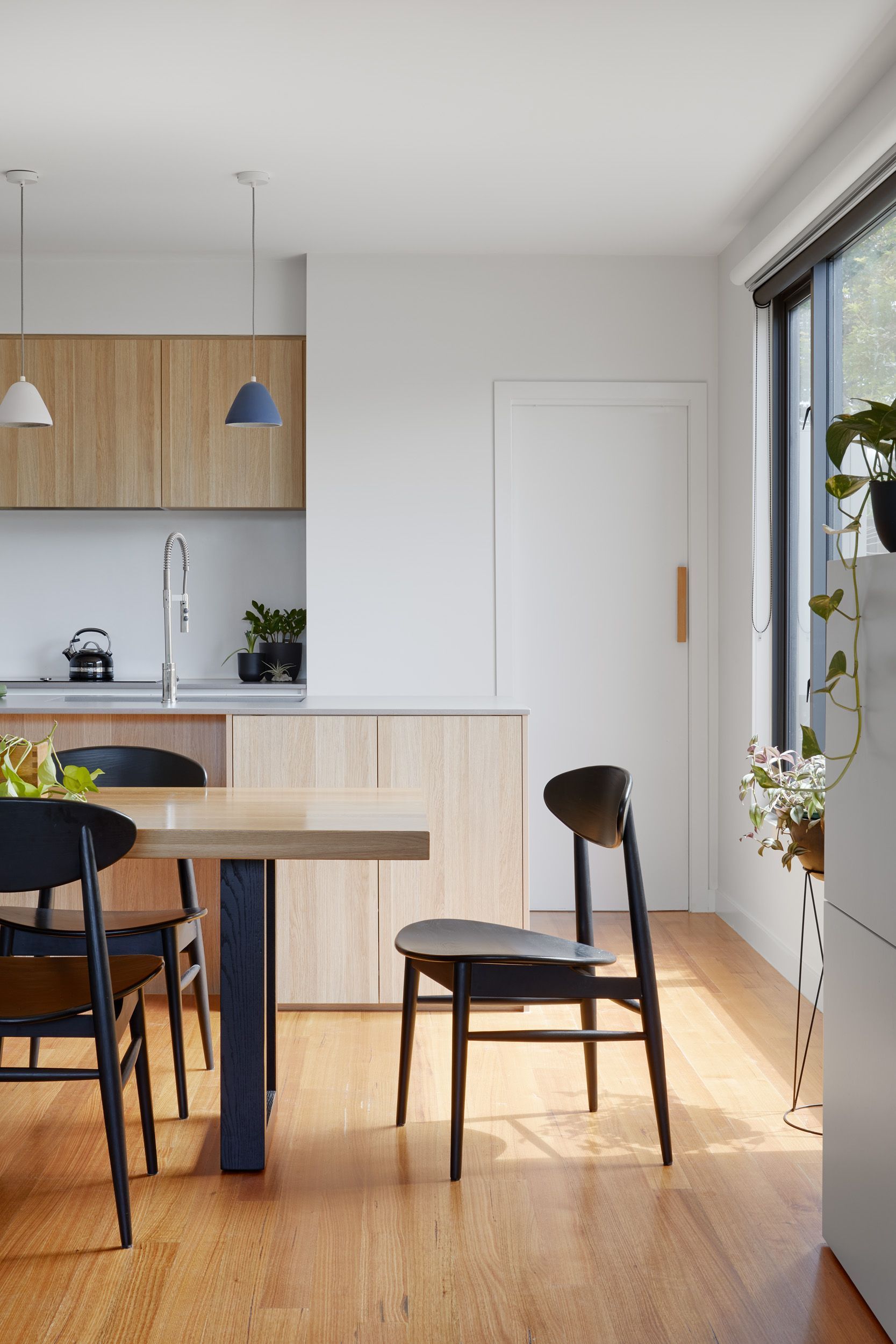 A dining room with a table and chairs and a kitchen in the background.