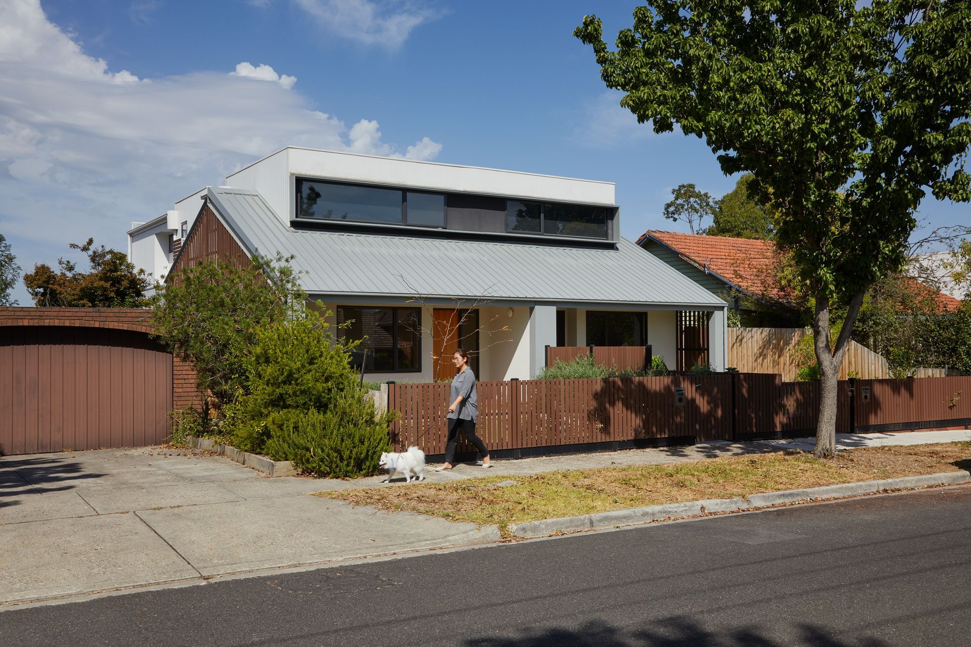 A woman walking a dog in front of a house