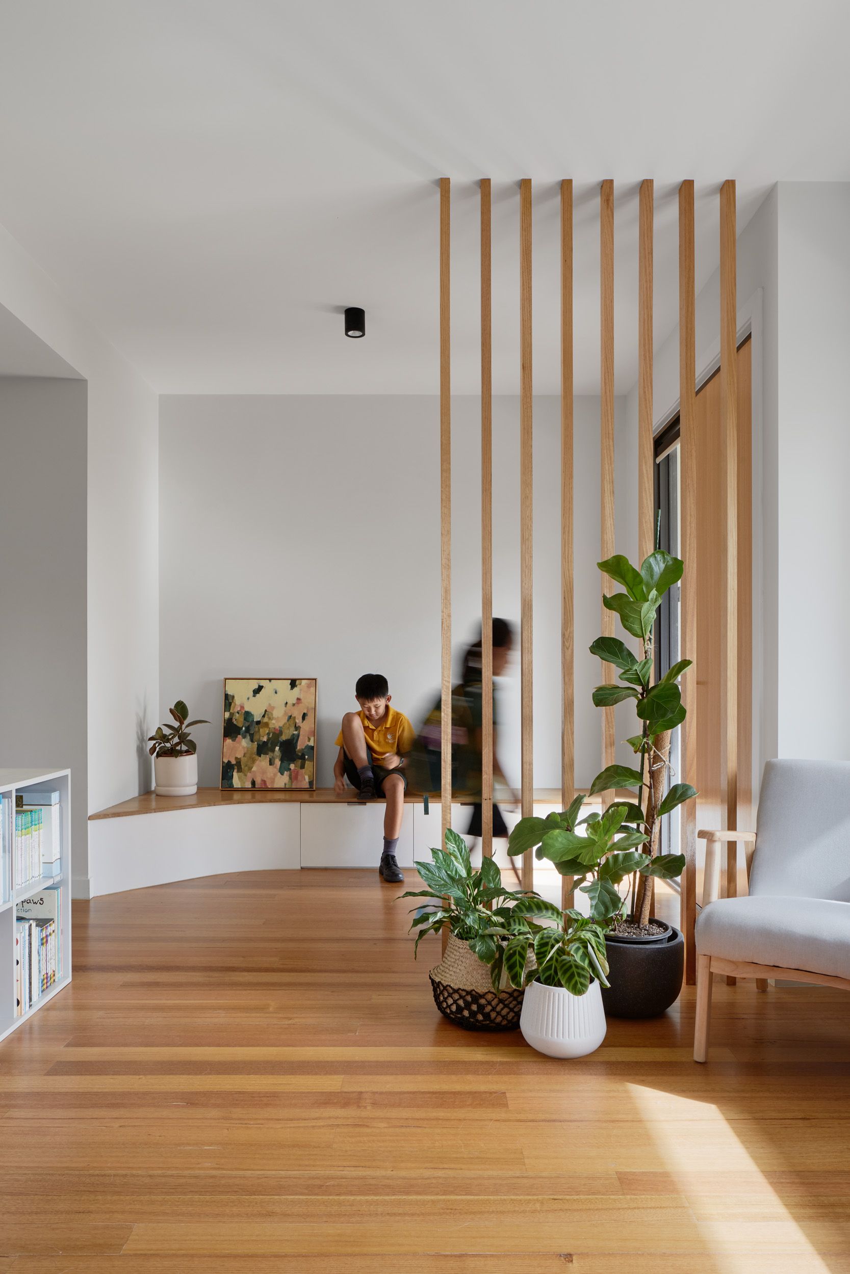 A person is sitting on a bench in a living room behind a wooden divider.