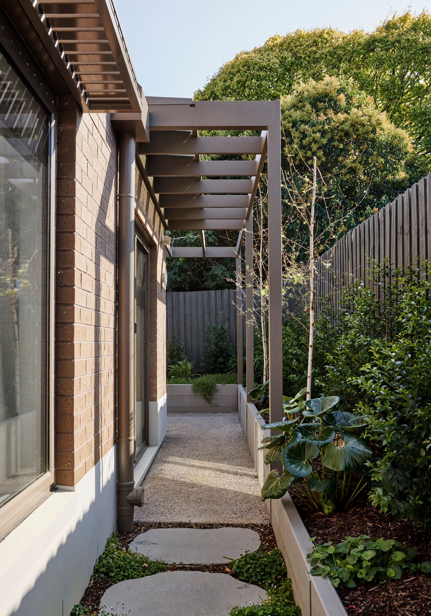 A walkway leading to a house with a pergola and a fence.