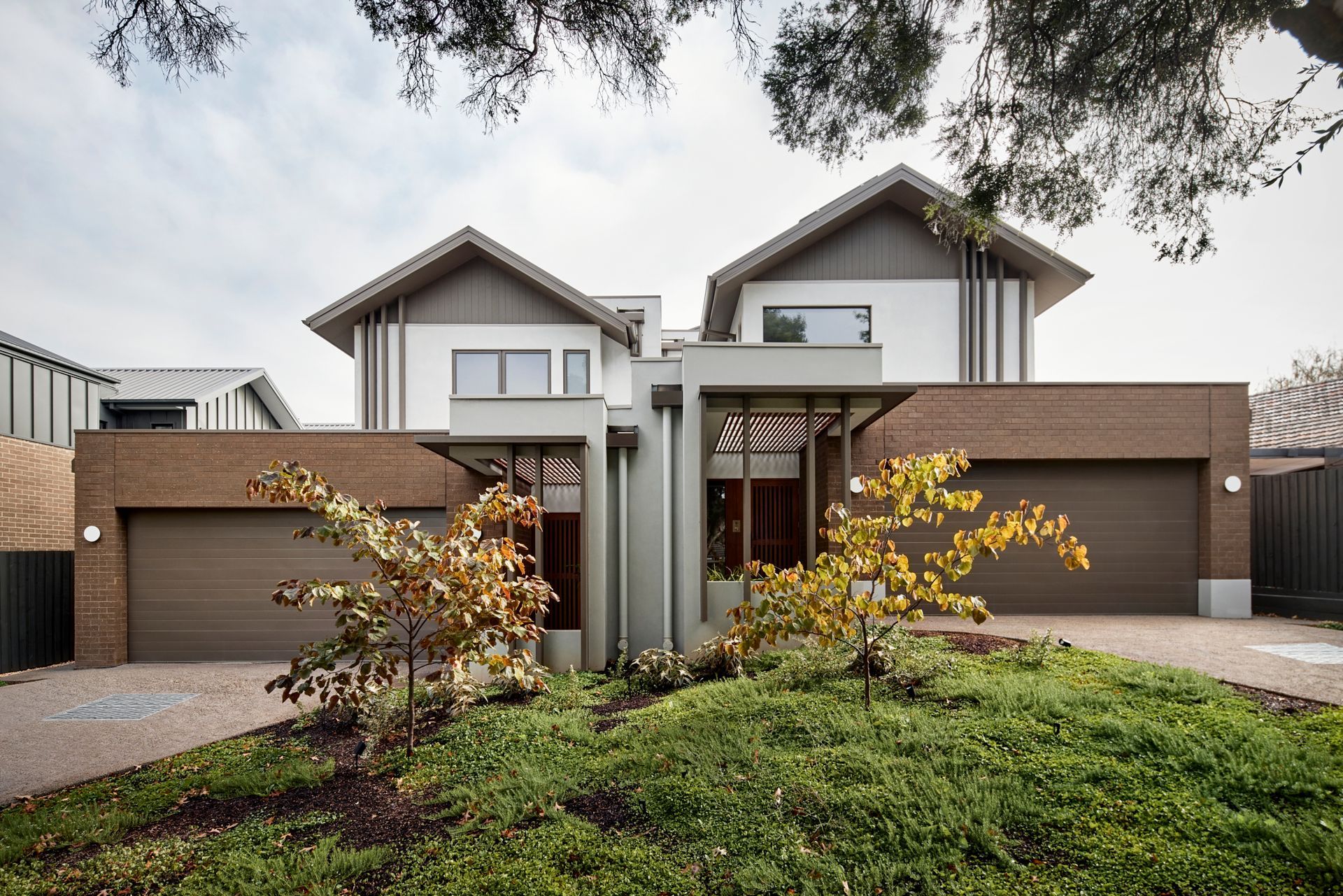 A large house with two garages is sitting on top of a lush green hill.