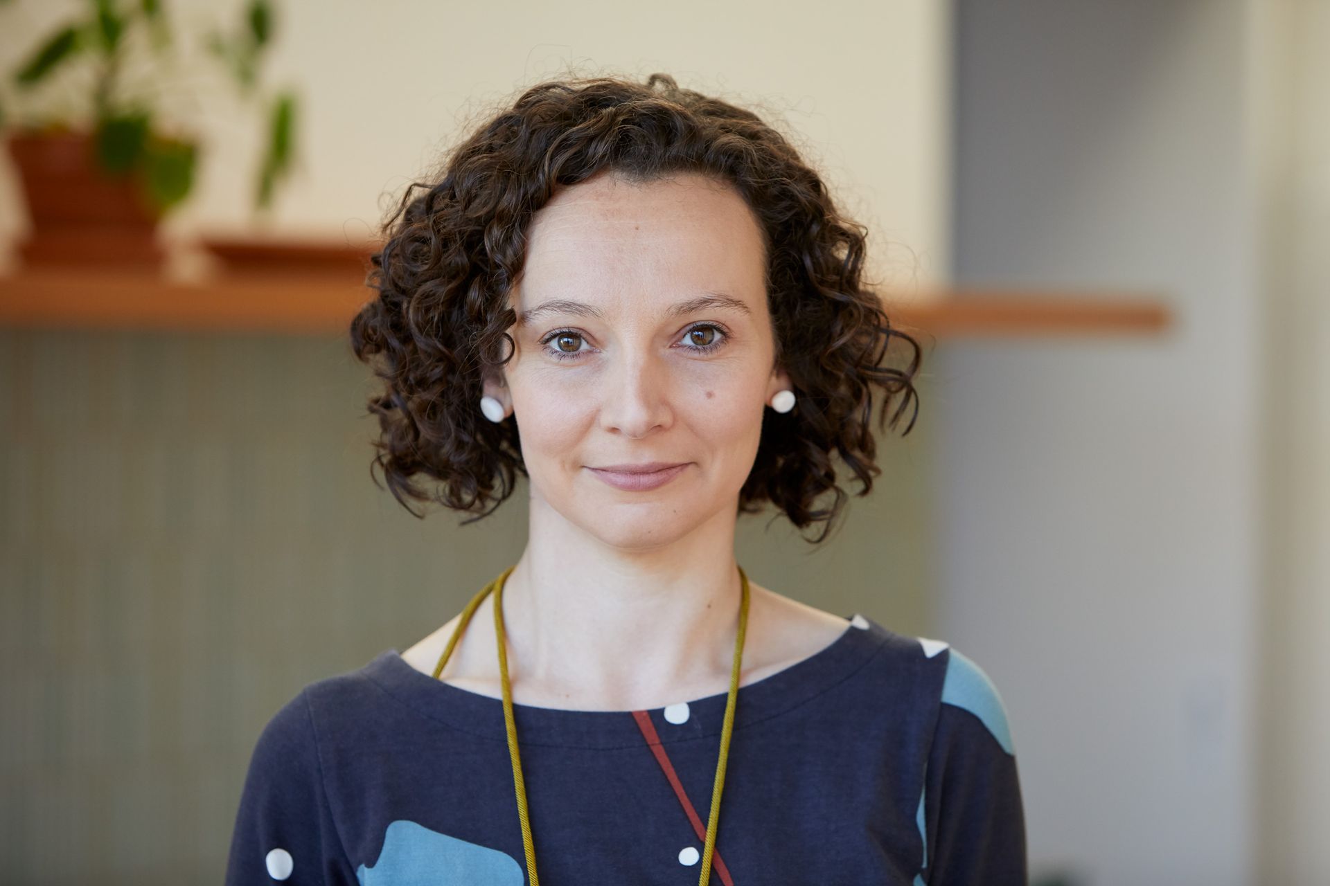 A woman with curly hair is smiling for the camera and wearing a necklace.