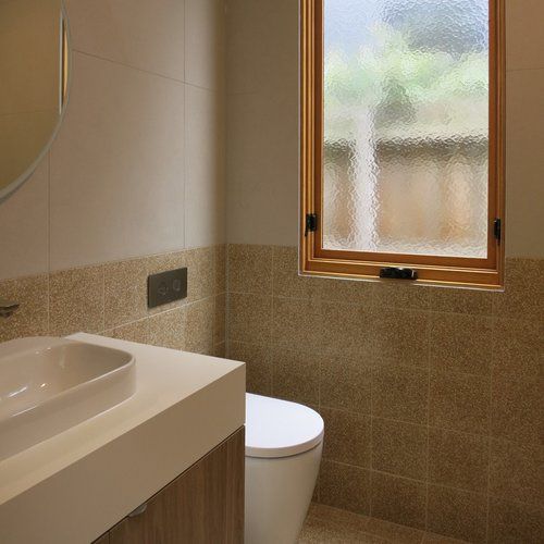 A bathroom with a toilet , sink , mirror and window