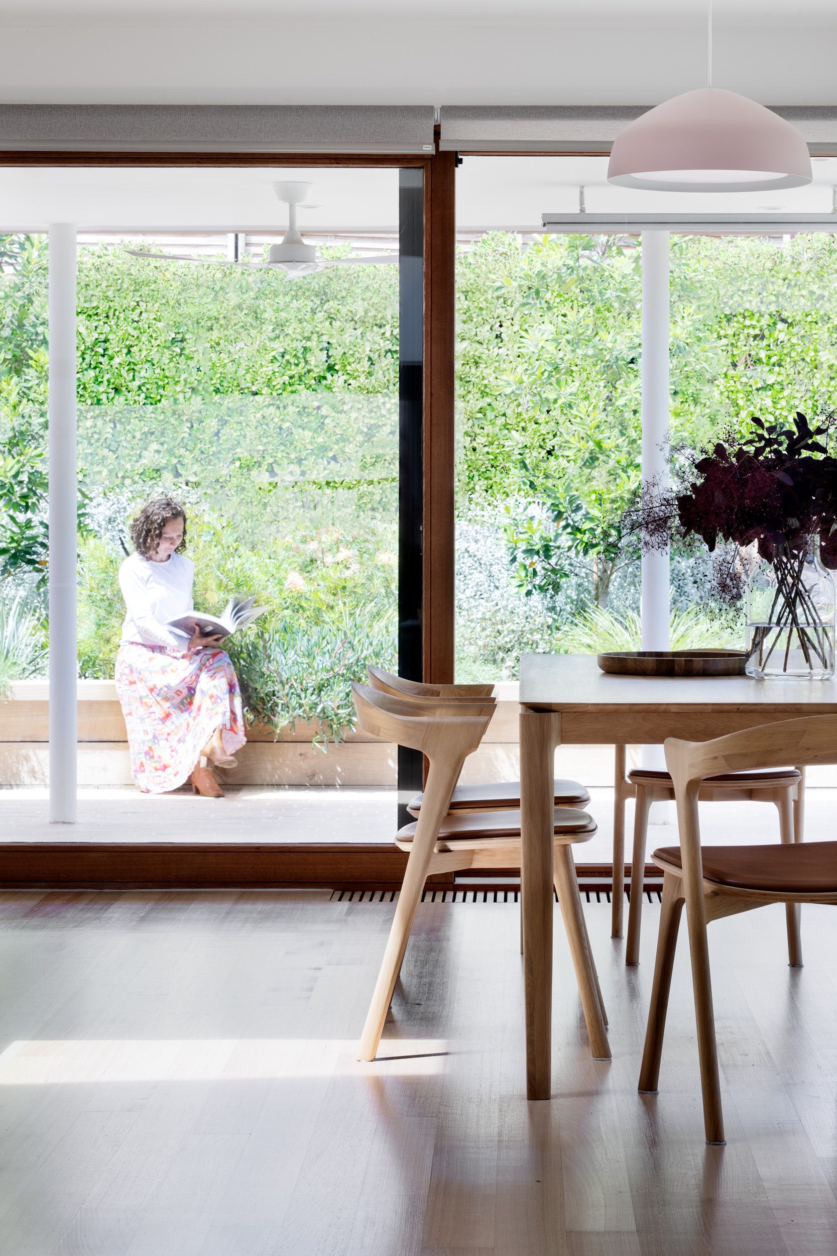 A woman is sitting on a bench in front of a sliding glass door in a dining room.
