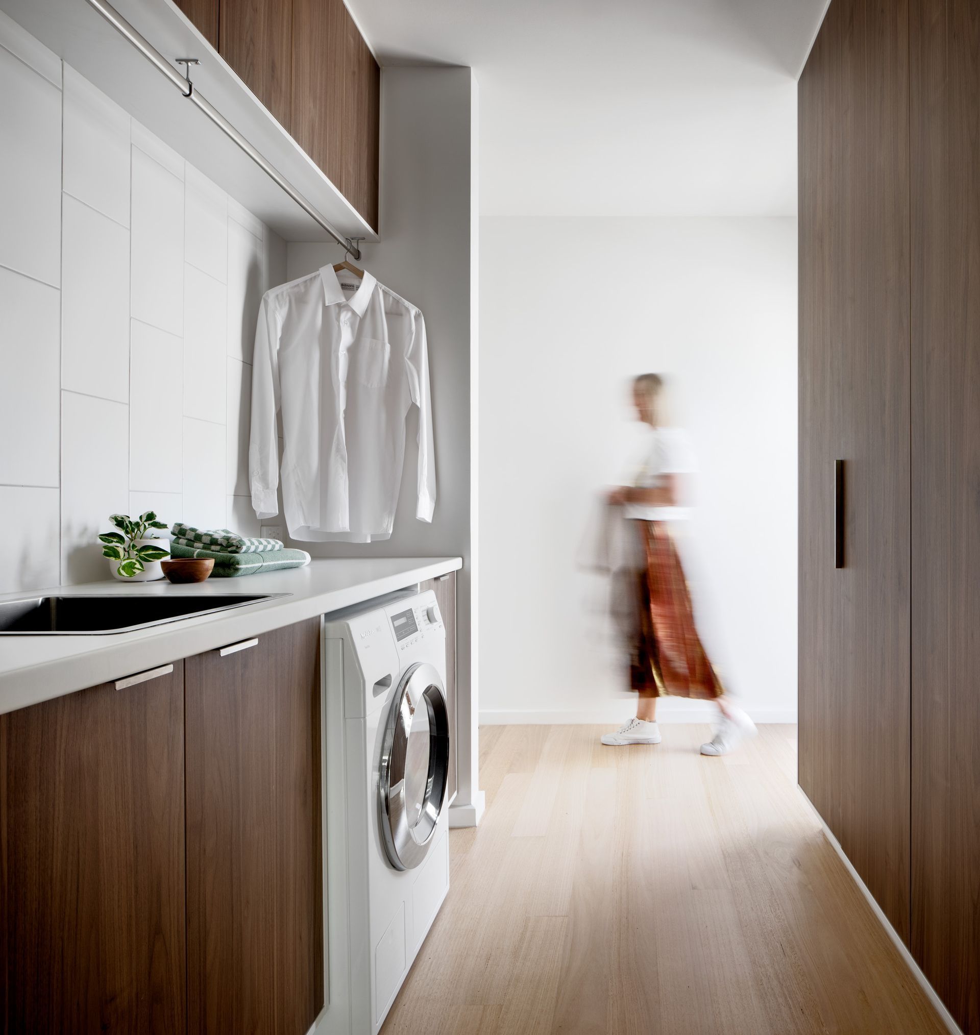 A laundry room with a washer and dryer and a person walking in the background