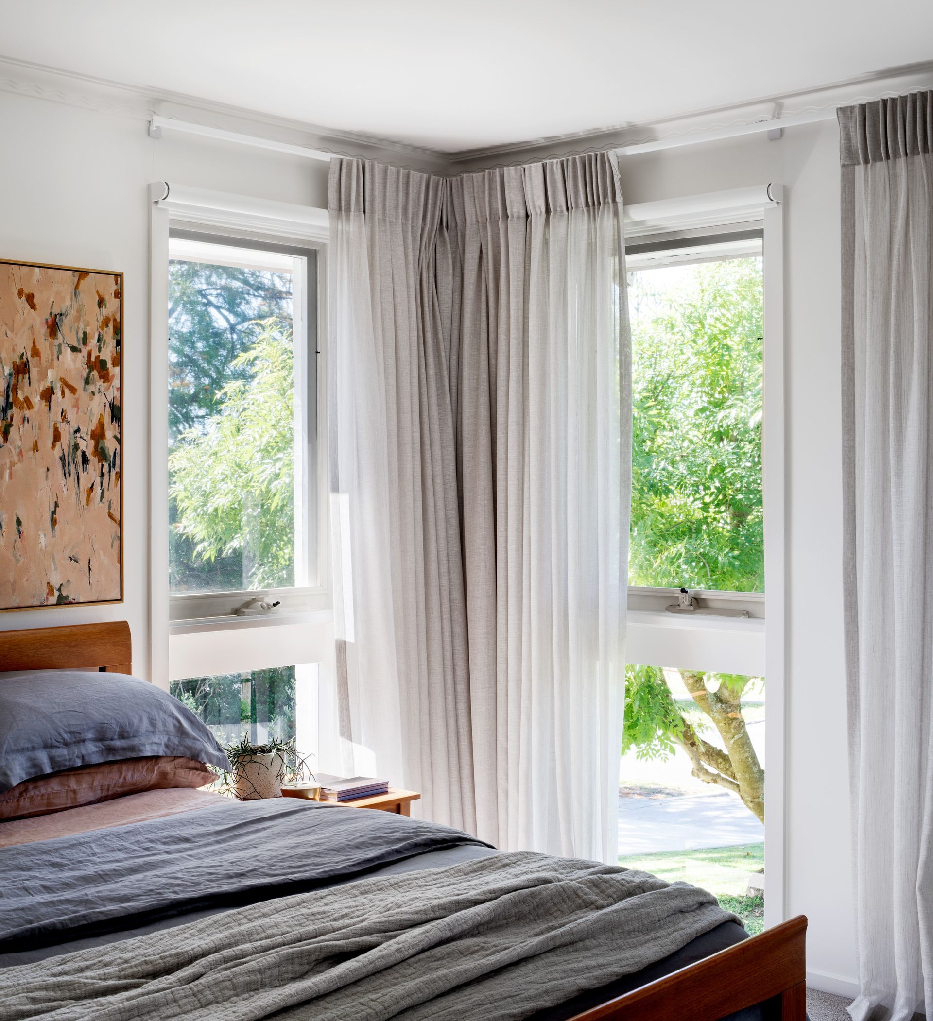 A bedroom with a bed , two windows and a painting on the wall.