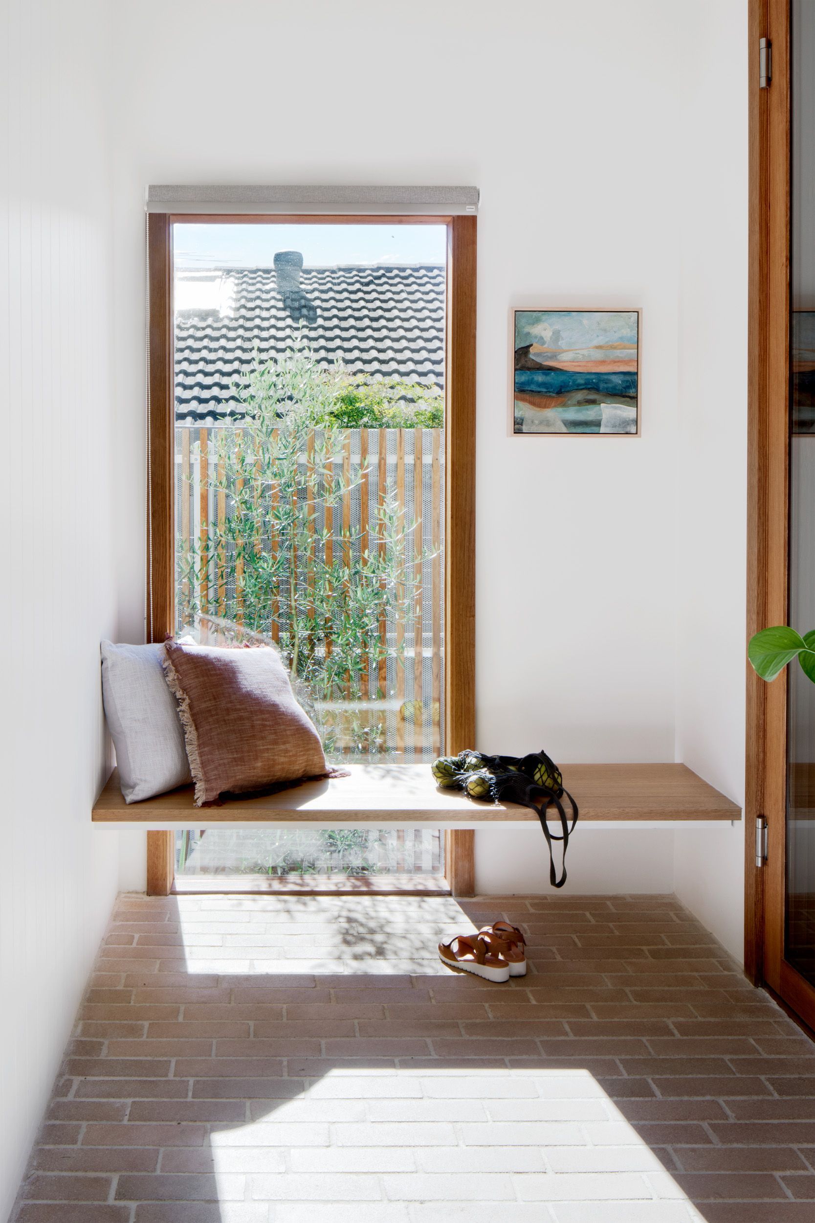 There is a bench in front of a window with a picture on the wall.