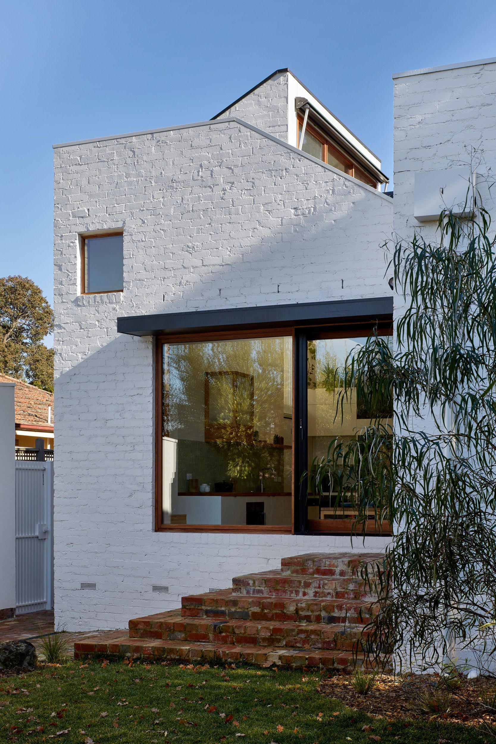 Exterior view of a modern white brick house with large glass windows and brick stairs leading up.