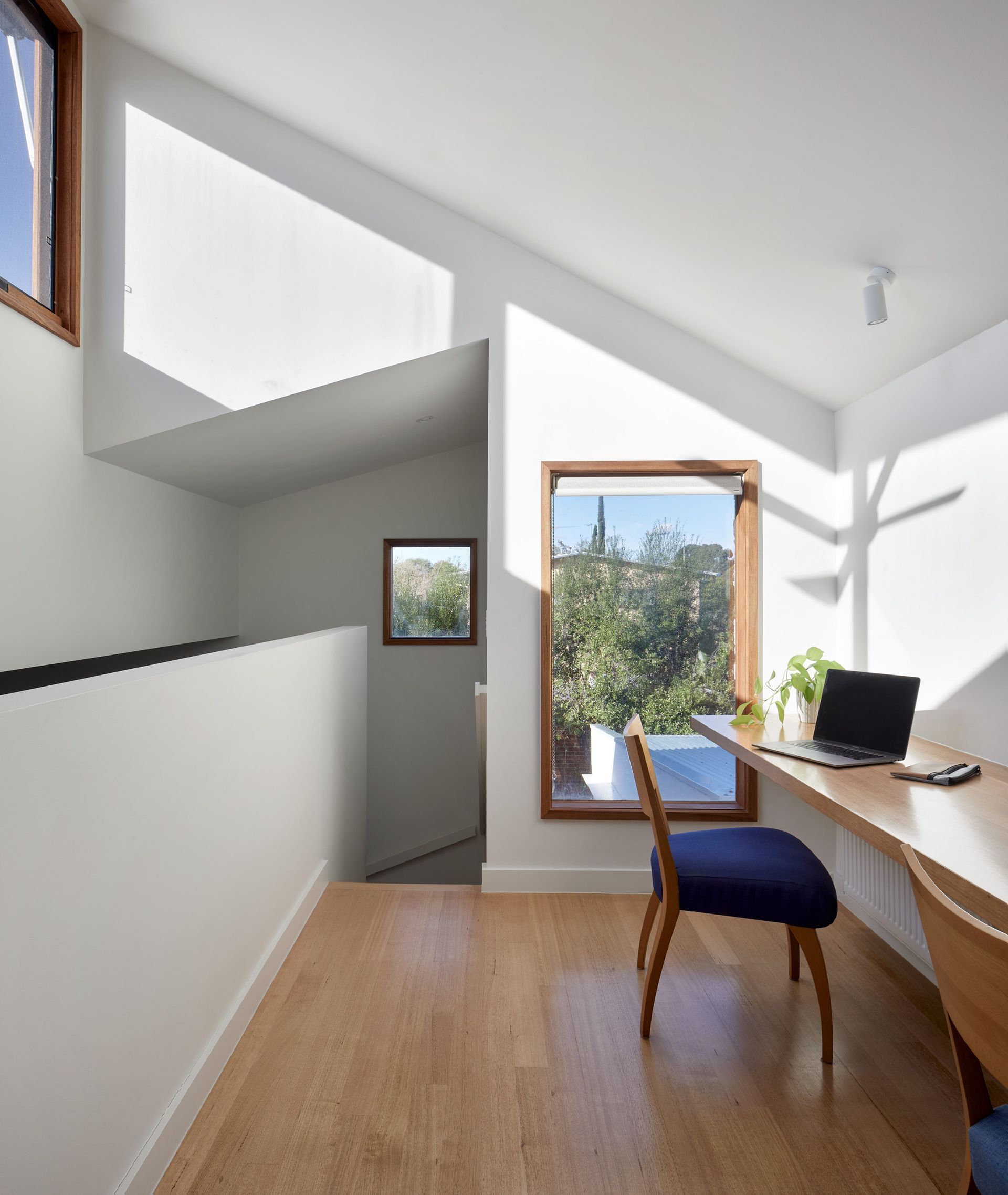 A bright home office with a wooden desk, a blue chair, and a laptop near a window overlooking greenery.