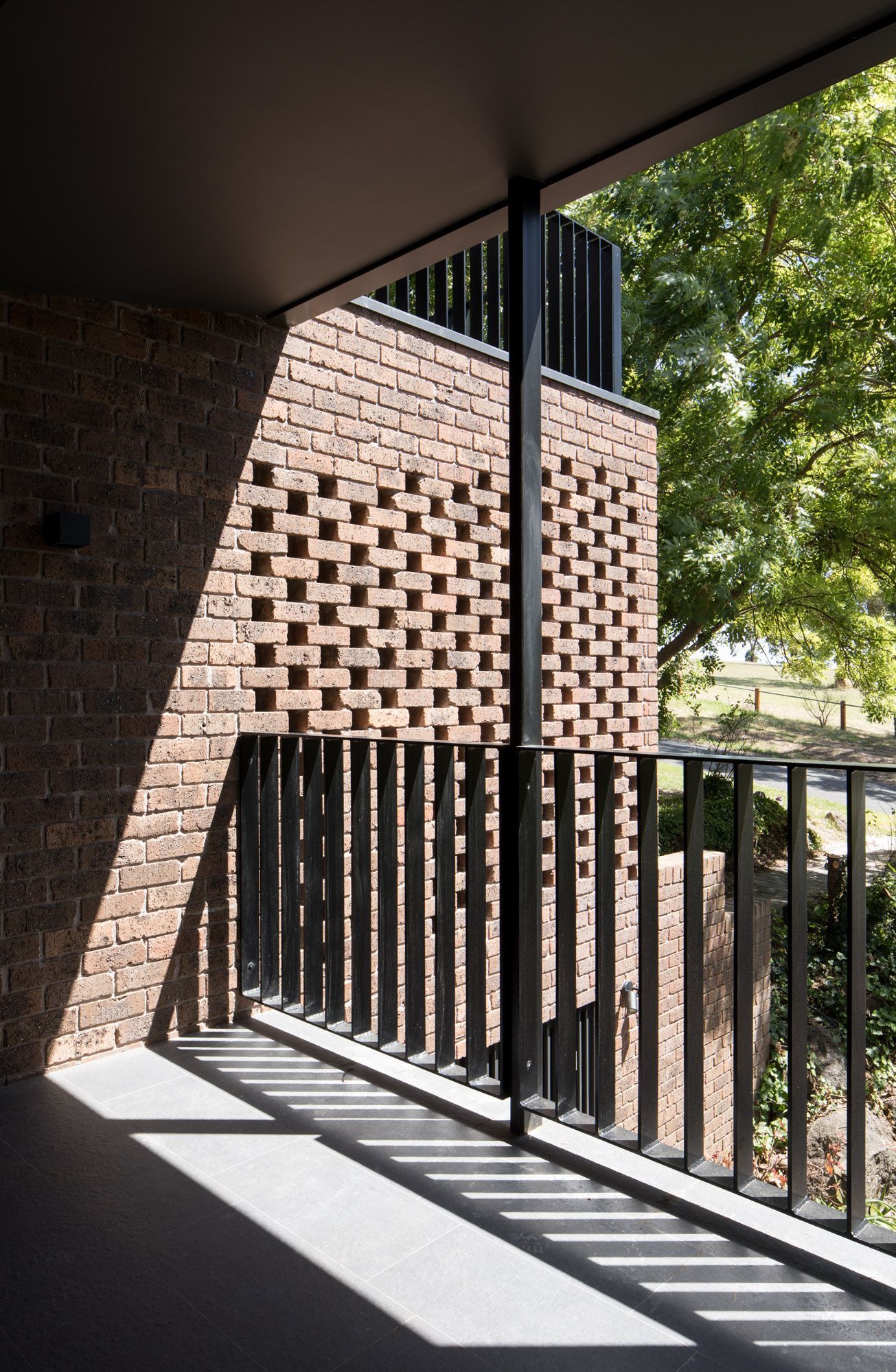 A balcony with a brick wall and a black railing.