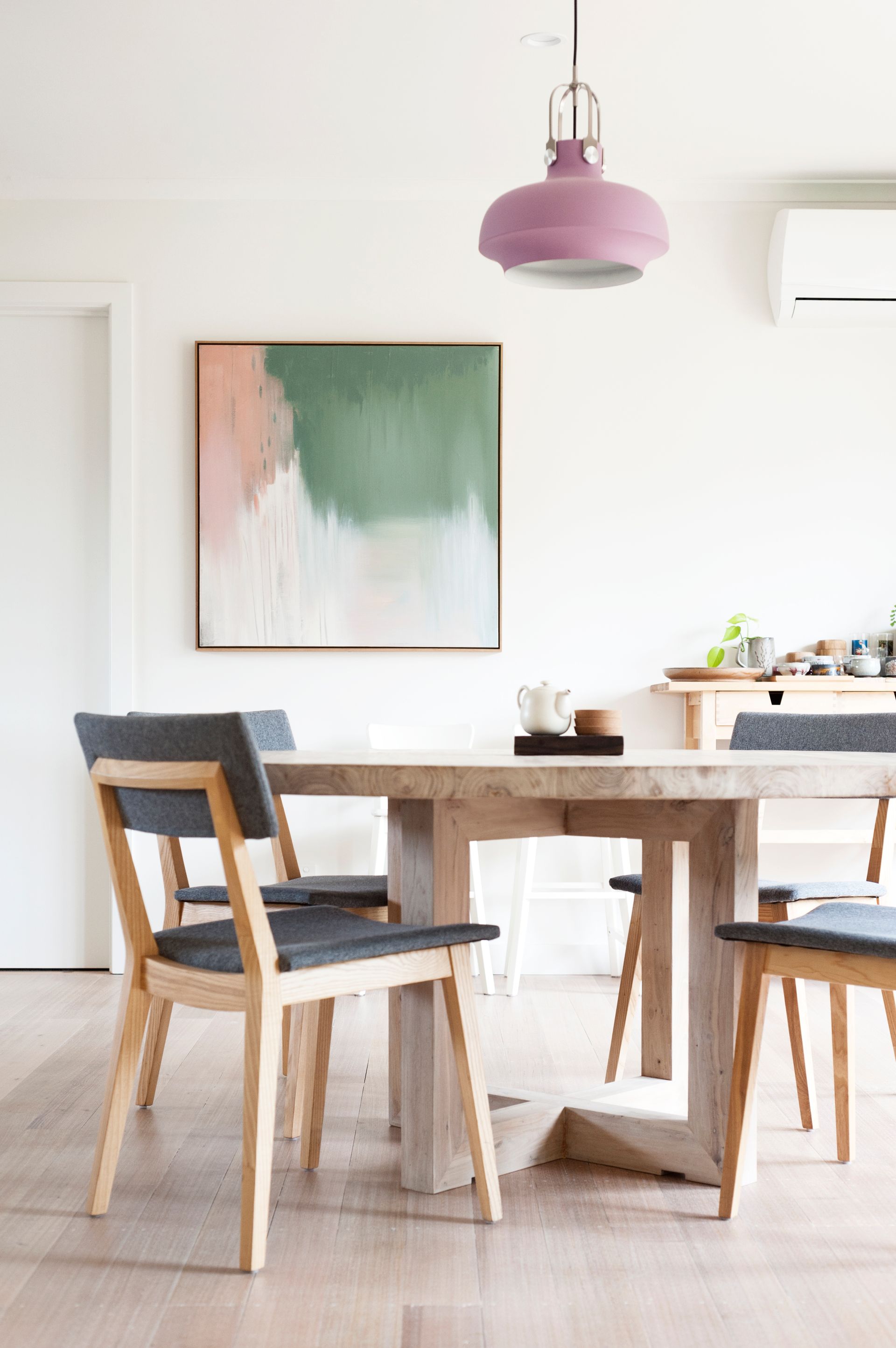 A dining room with a table and chairs and a painting on the wall.