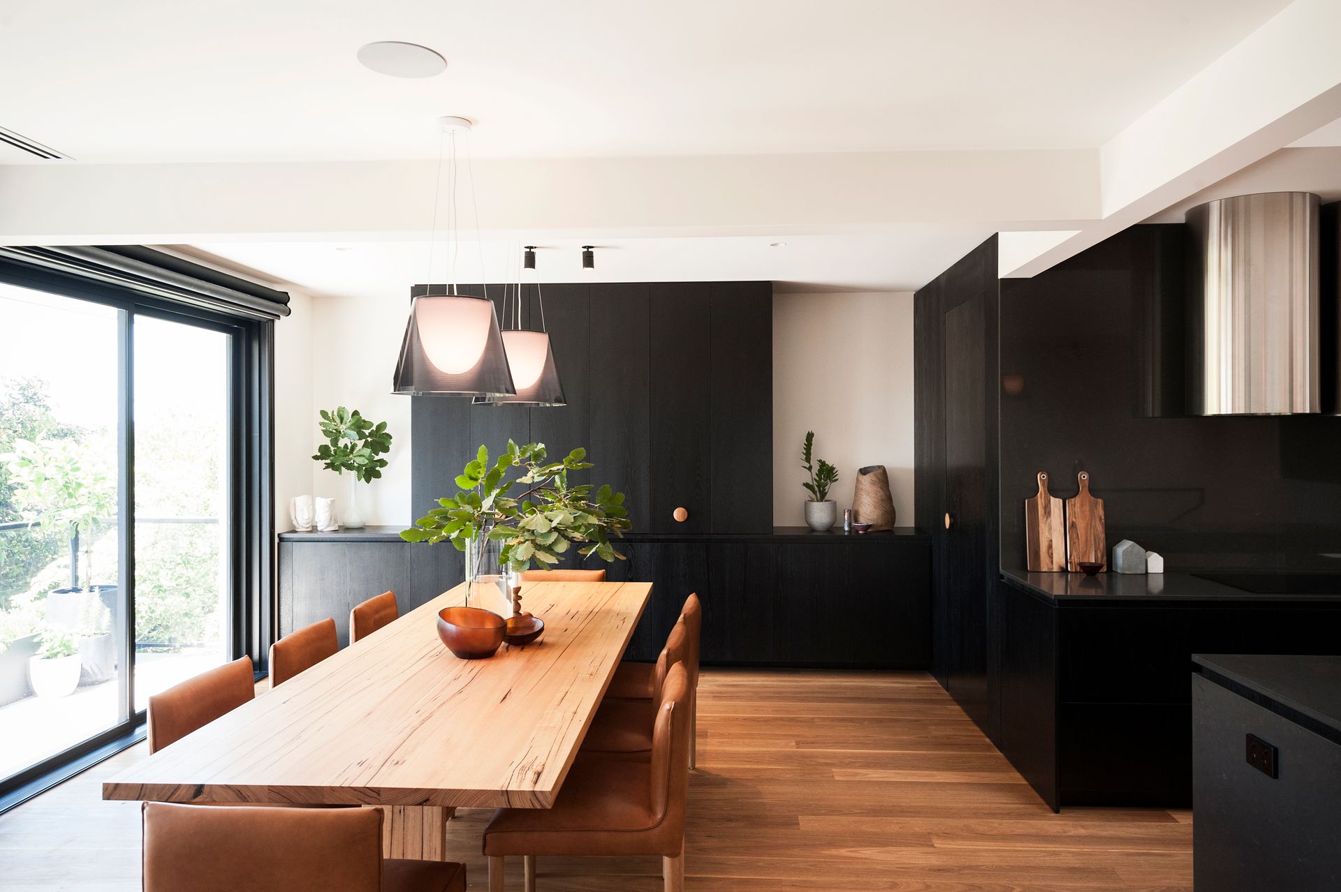 A dining room with a wooden table and chairs and a black kitchen.