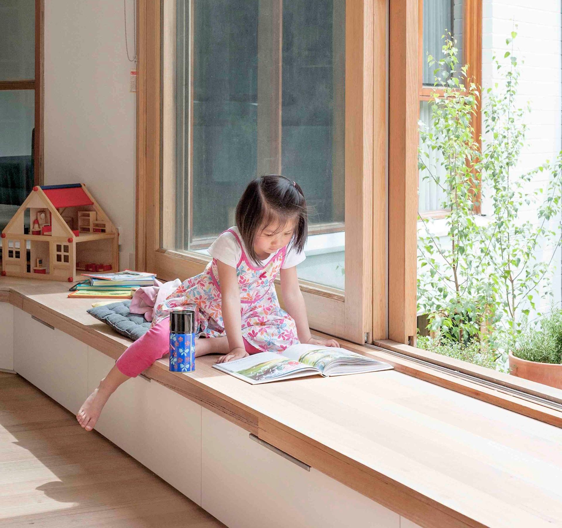 A little girl is sitting on a window sill reading a book
