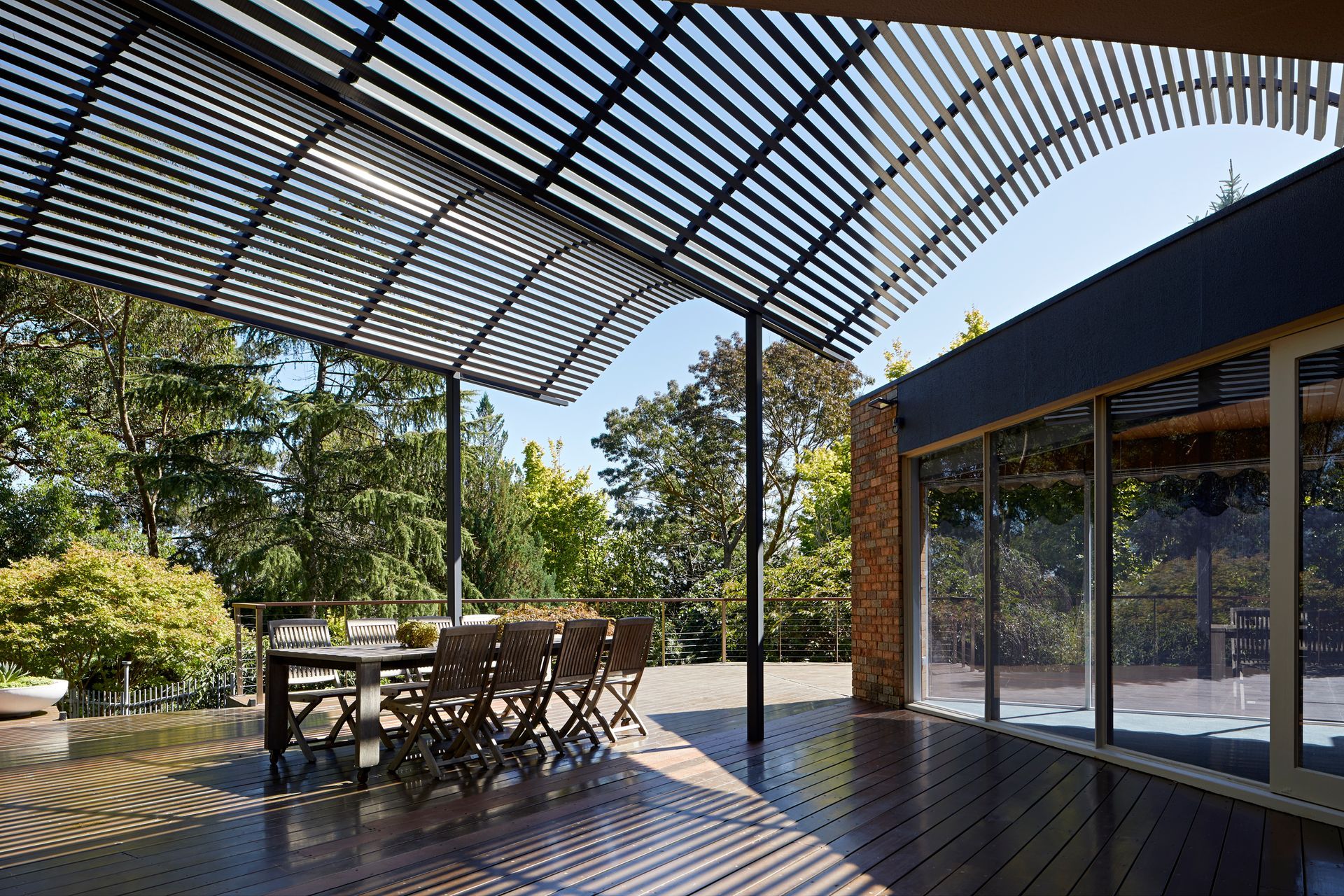 A wooden deck with a table and chairs under a pergola.