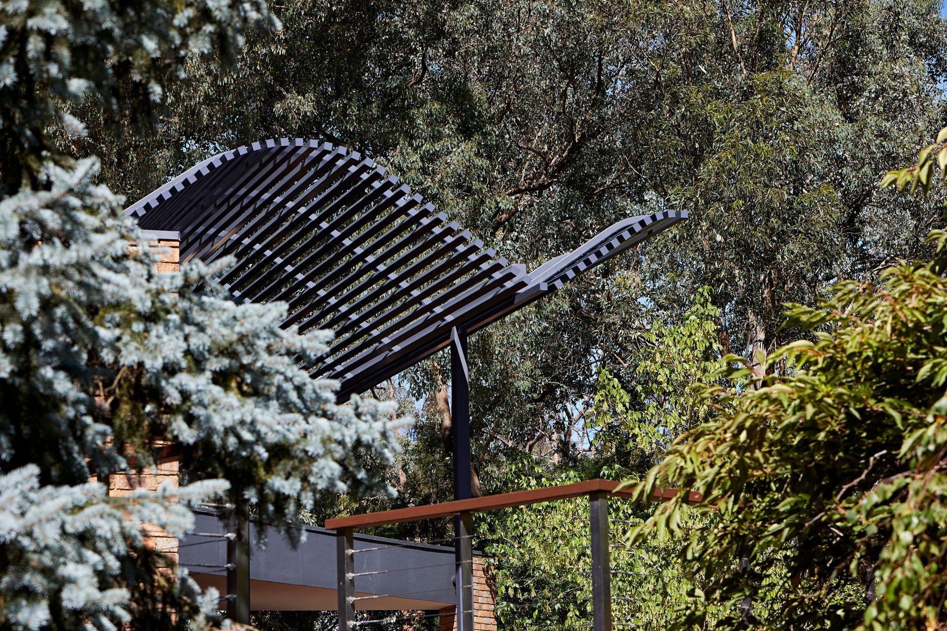 A black pergola is surrounded by trees in a garden.