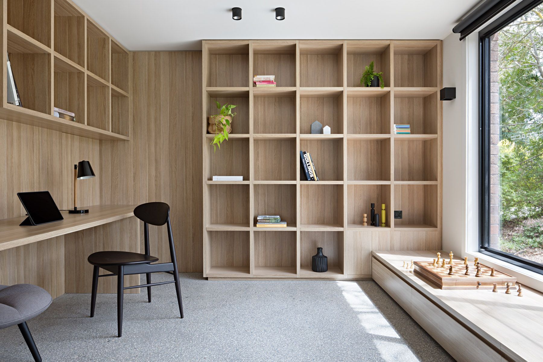 A room with a desk , chair , shelves and a window.