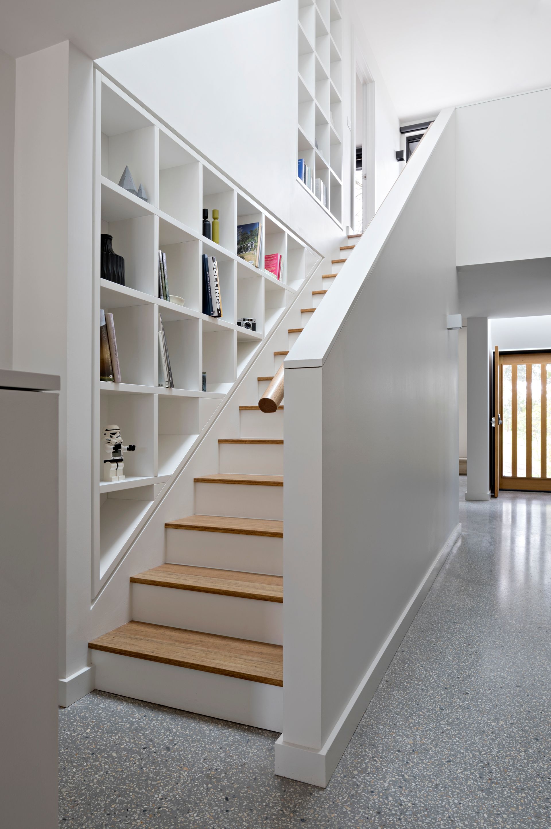 A white staircase with wooden steps and shelves underneath it.
