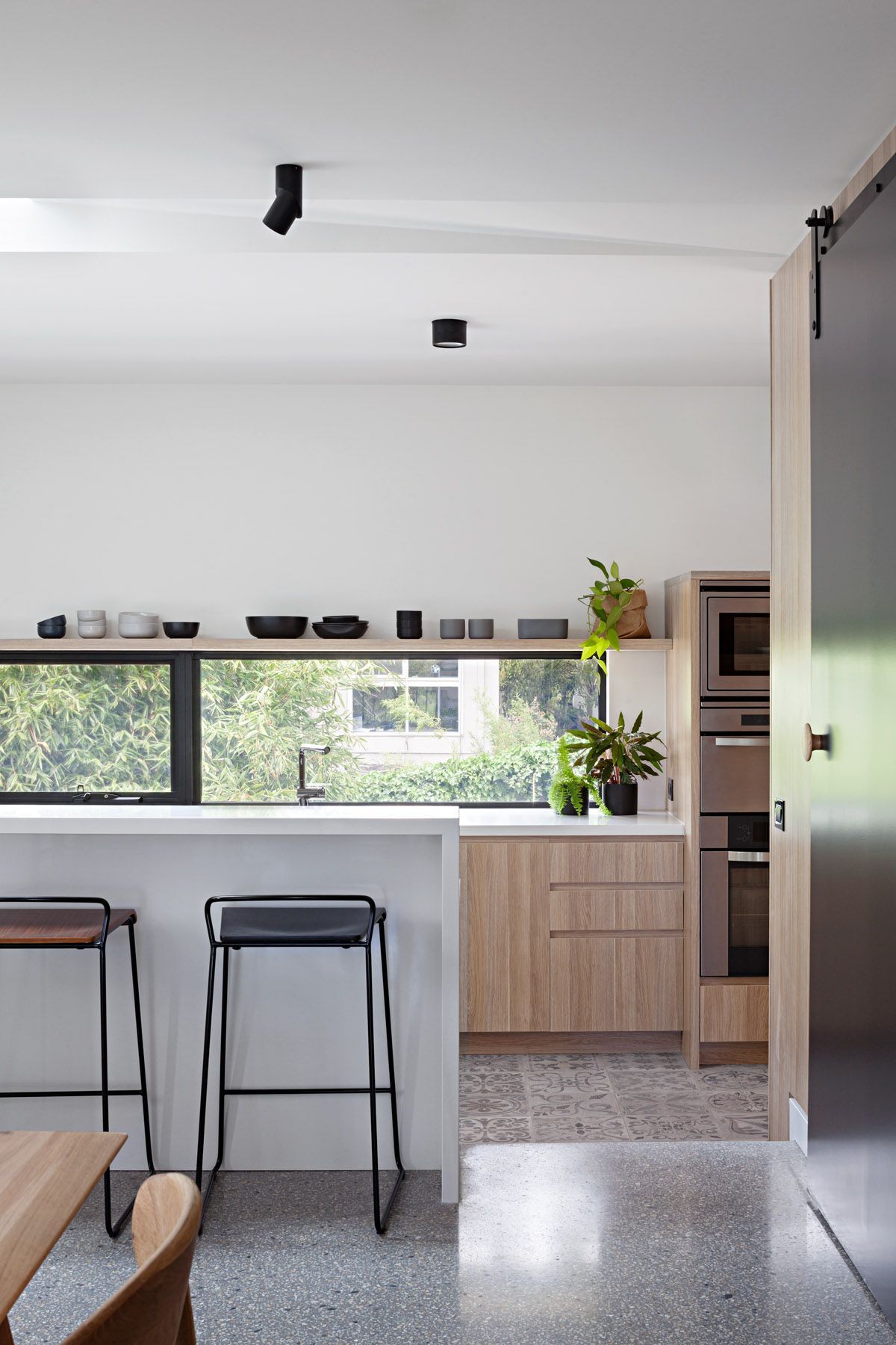 A kitchen with wooden cabinets and stools and a large window.