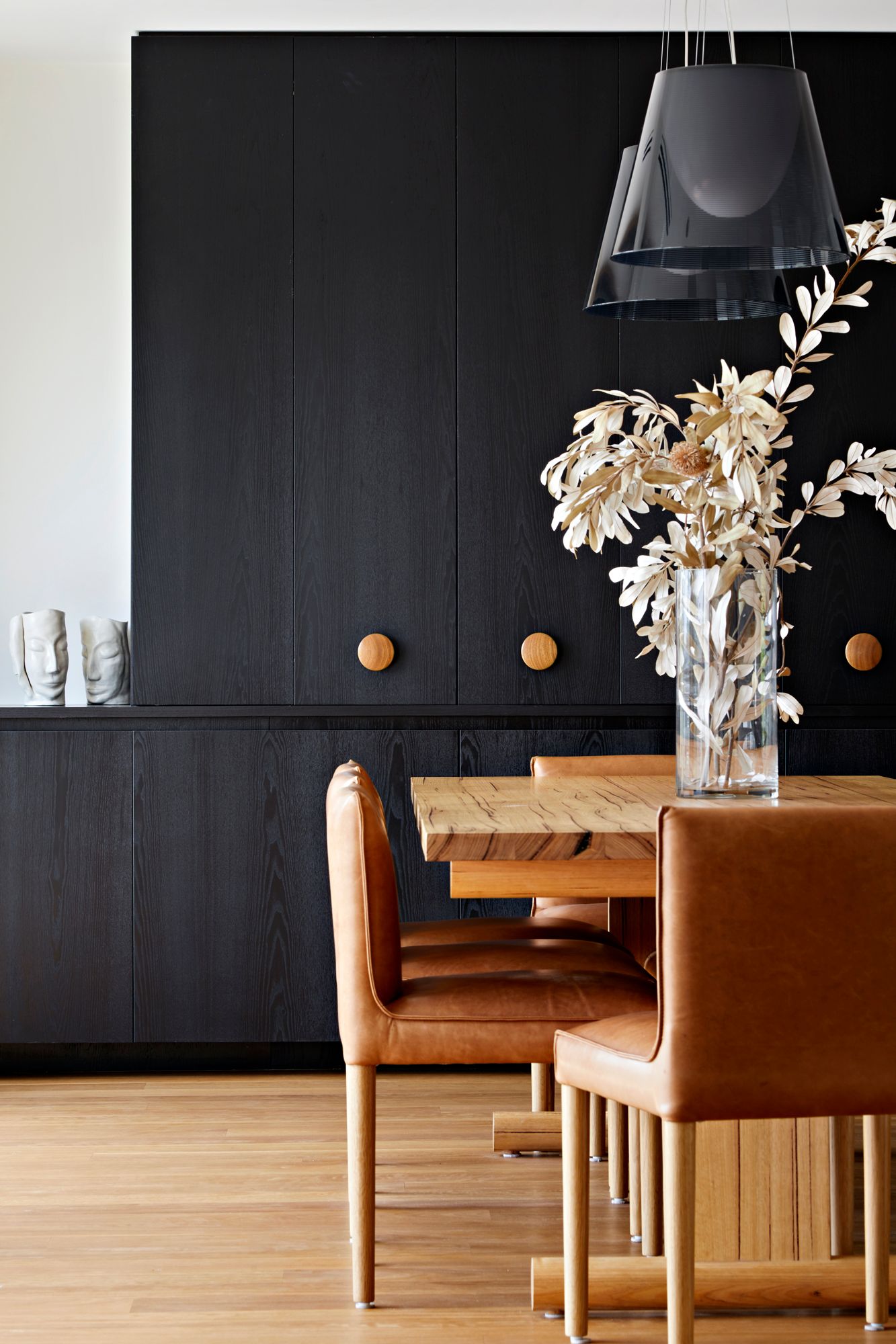 A dining room with a table and chairs and a vase of flowers on the table.