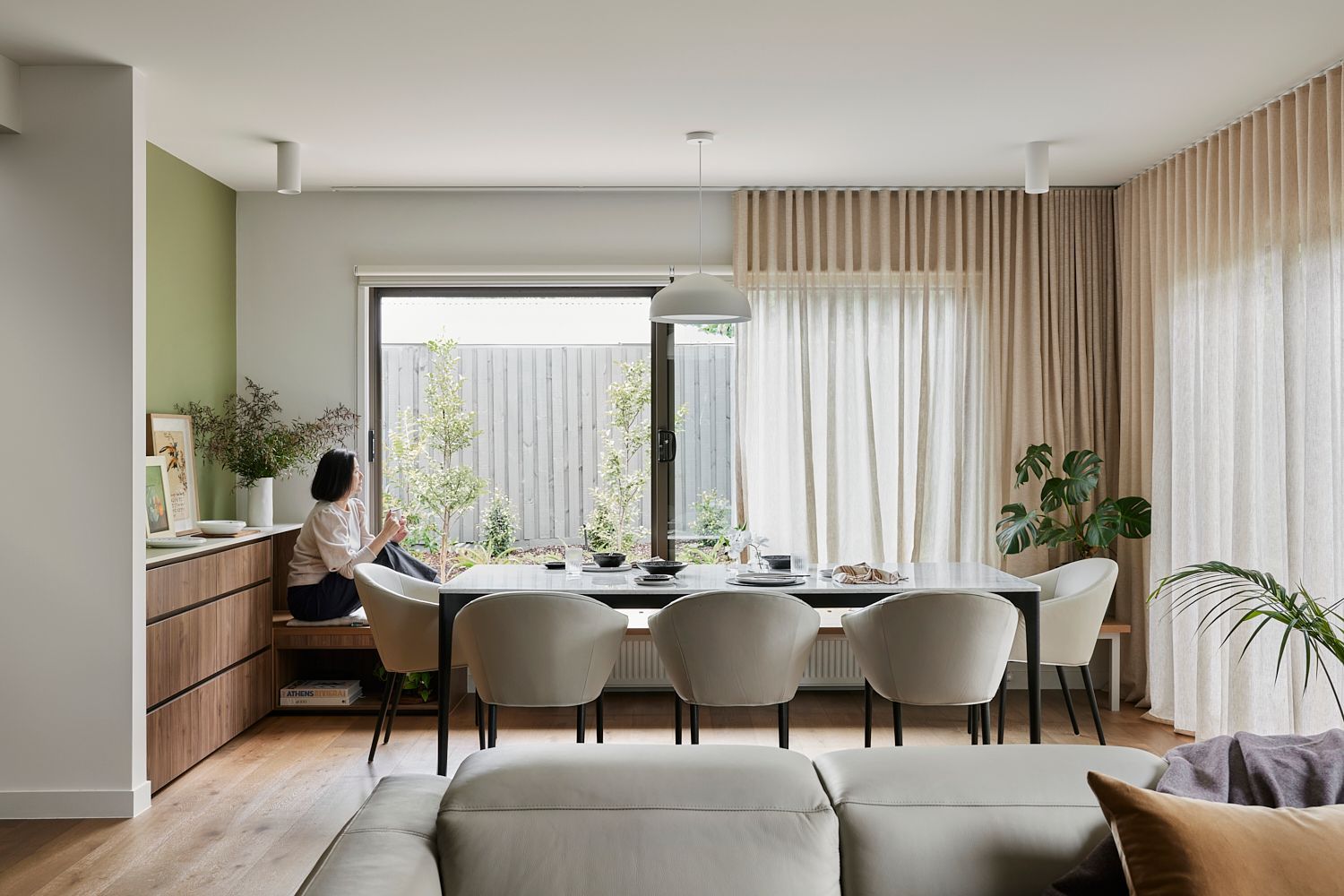 A woman is sitting on a bench in a living room next to a dining table.